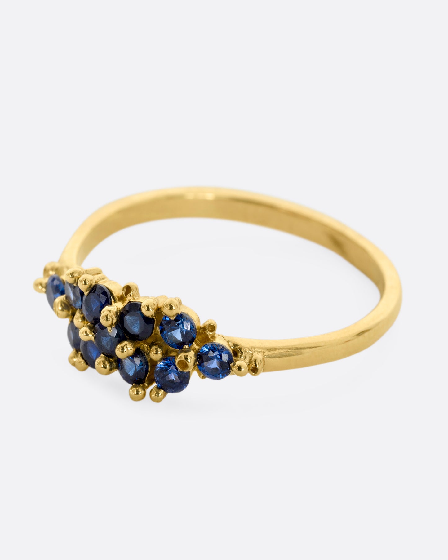 A yellow gold ring with a cluster of eleven blue sapphires. Shown from the side.