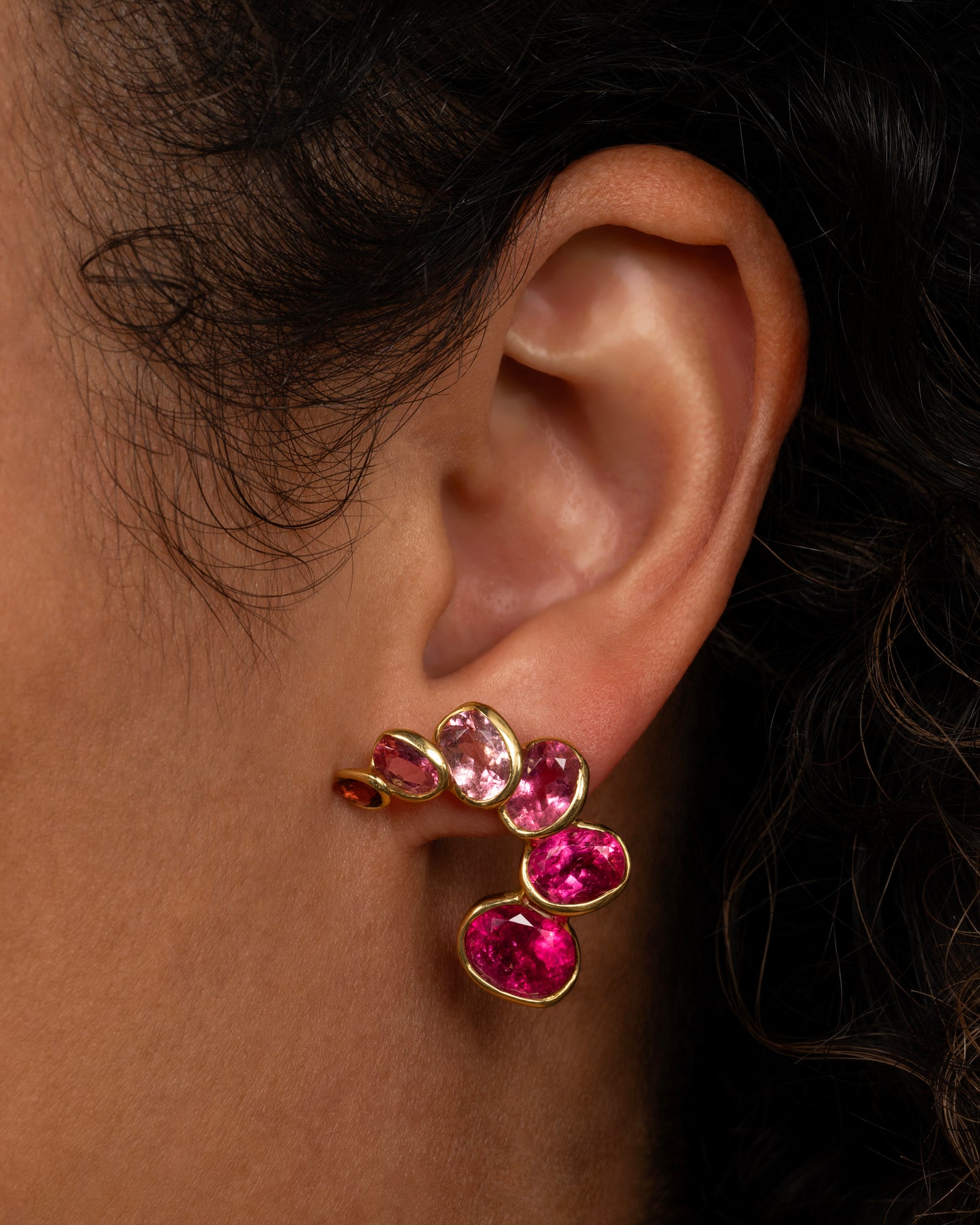 A pair of curved earrings with ombré pink tourmalines, shown on an ear.