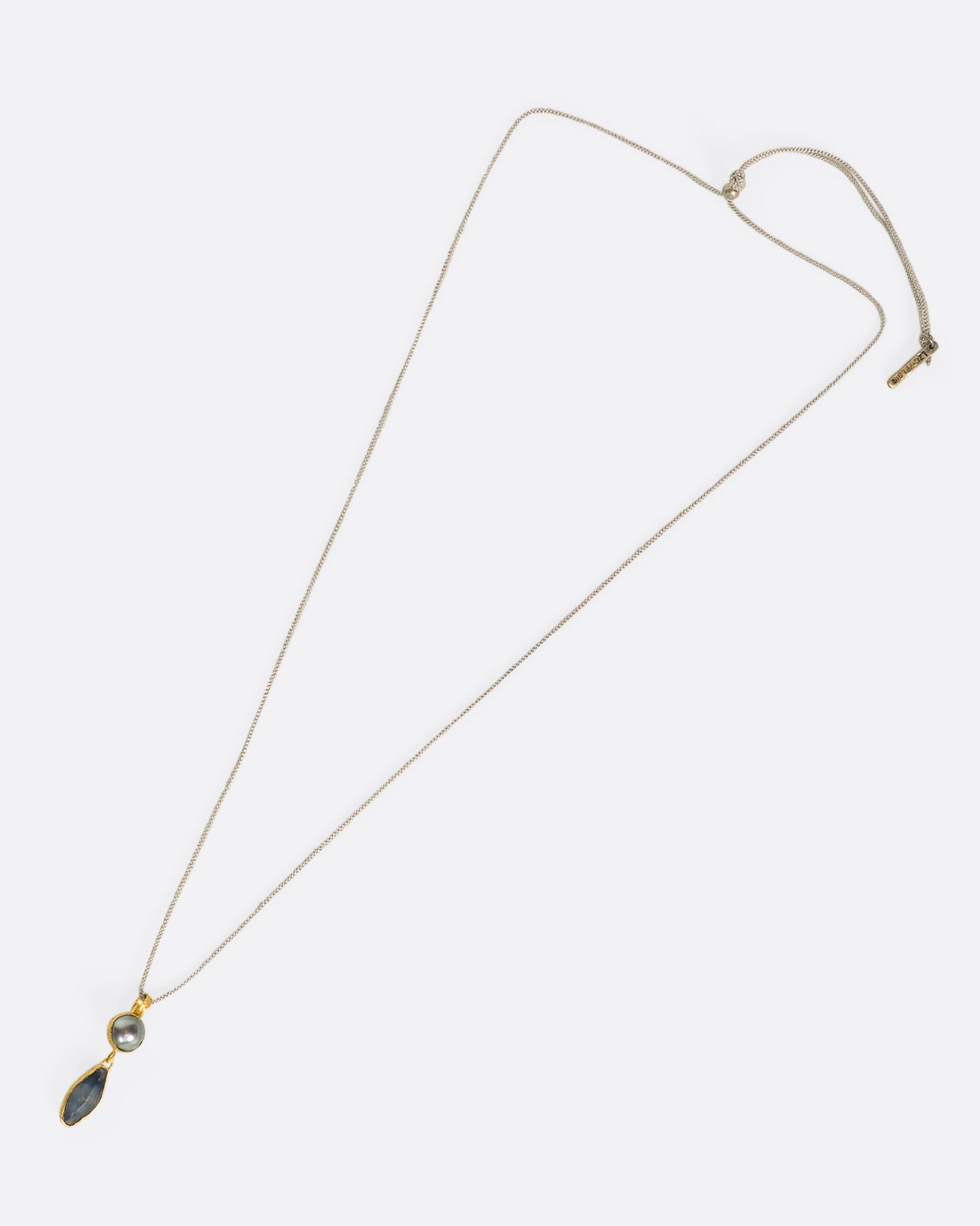 An overhead view of a yellow gold pendant with a pearl and Sri Lankan sapphire on a cord laying down flat..