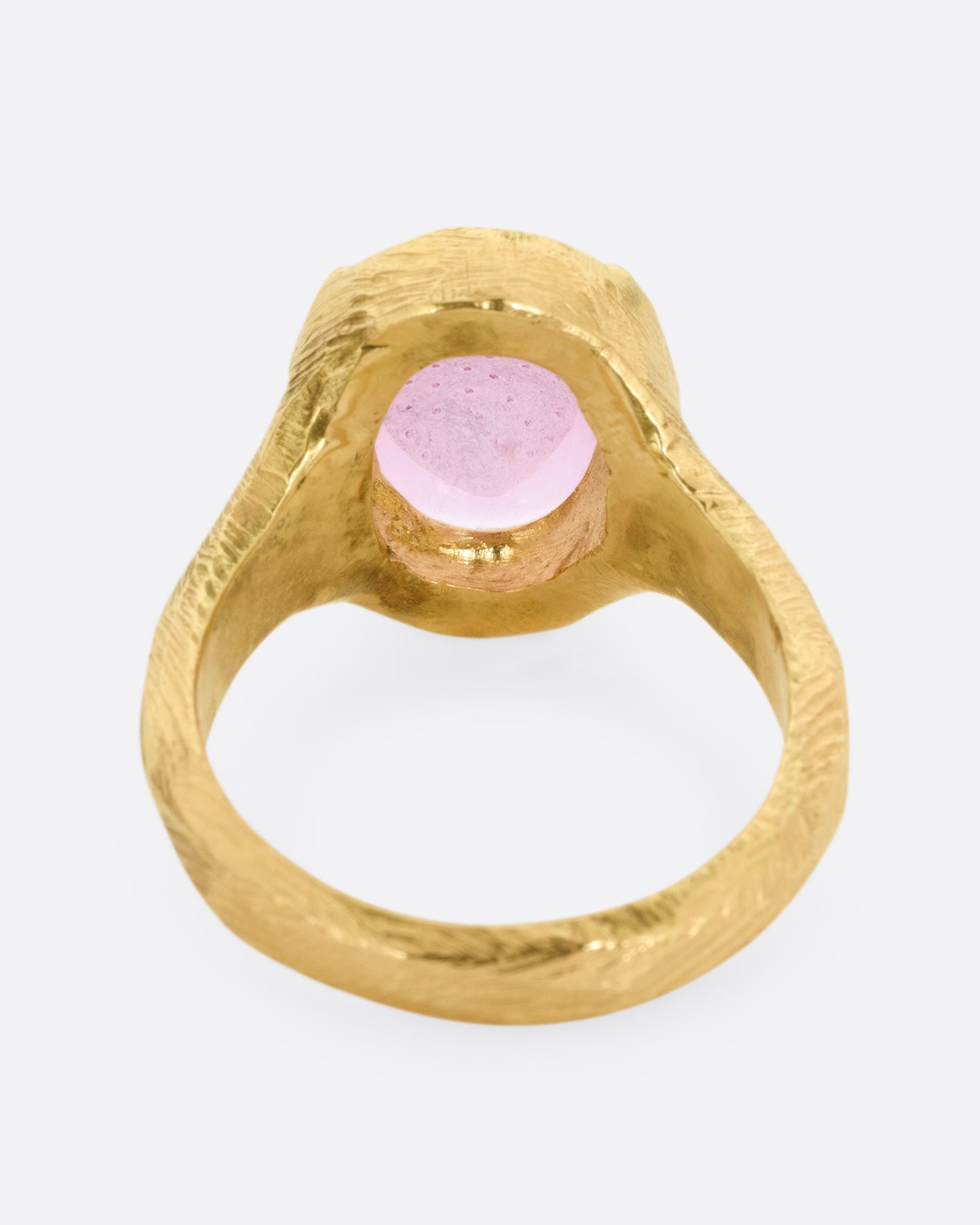 A yellow gold signet ring with a carved strawberry in a prong set pink garnet. Shown from the back.