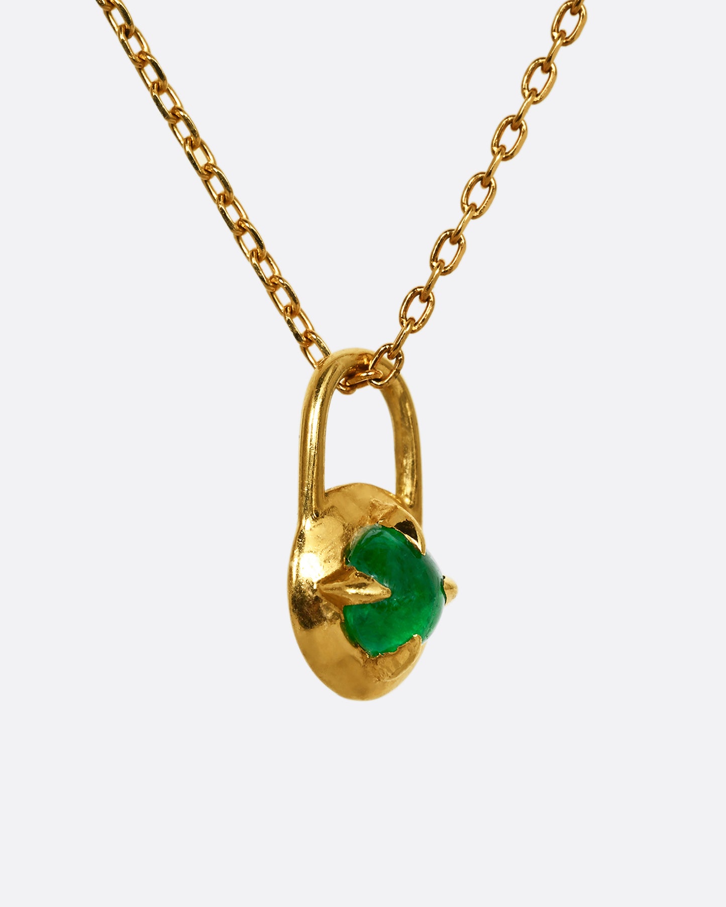 A yellow gold pendant in the shape of a lock with an emerald cabochon at the center. Shown on a chain, from the side.