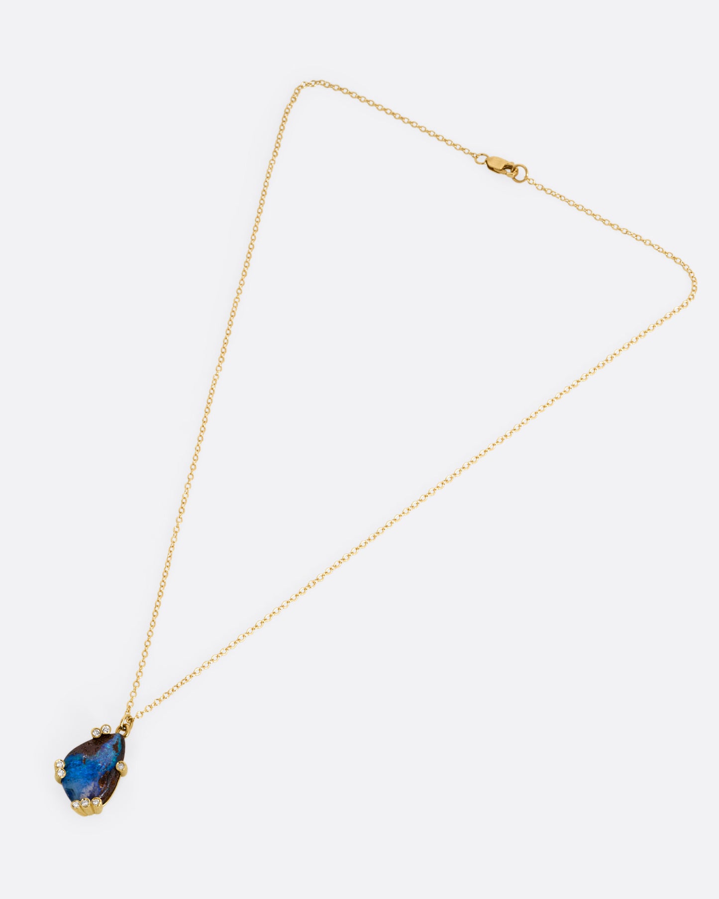 A yellow gold cable chain necklace with diamond studded gold anemones around a free-form boulder opal pendant, shown from the front.