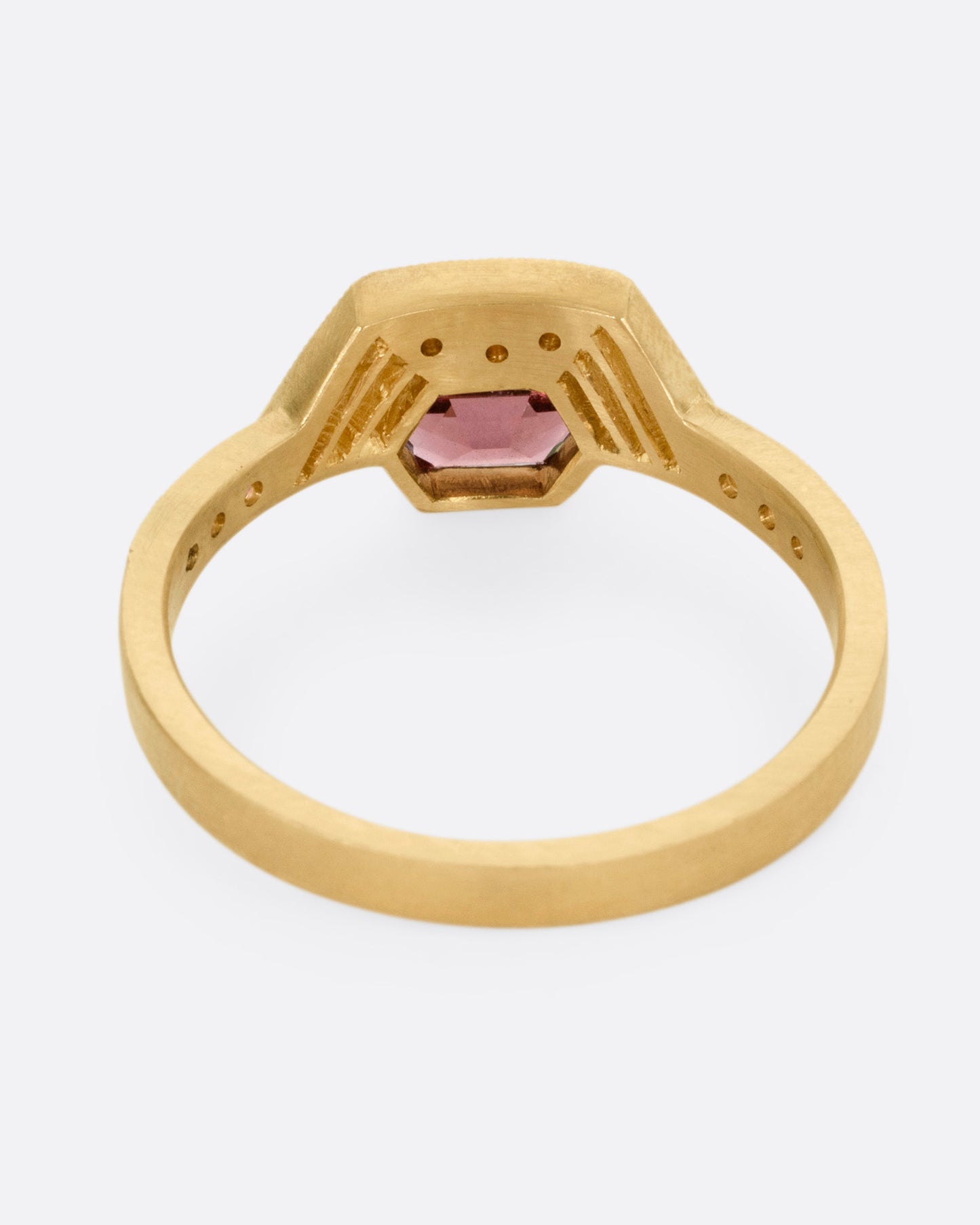 A yellow gold ring with diamond accents, linear cutouts, and a red spinel, shown from the back.