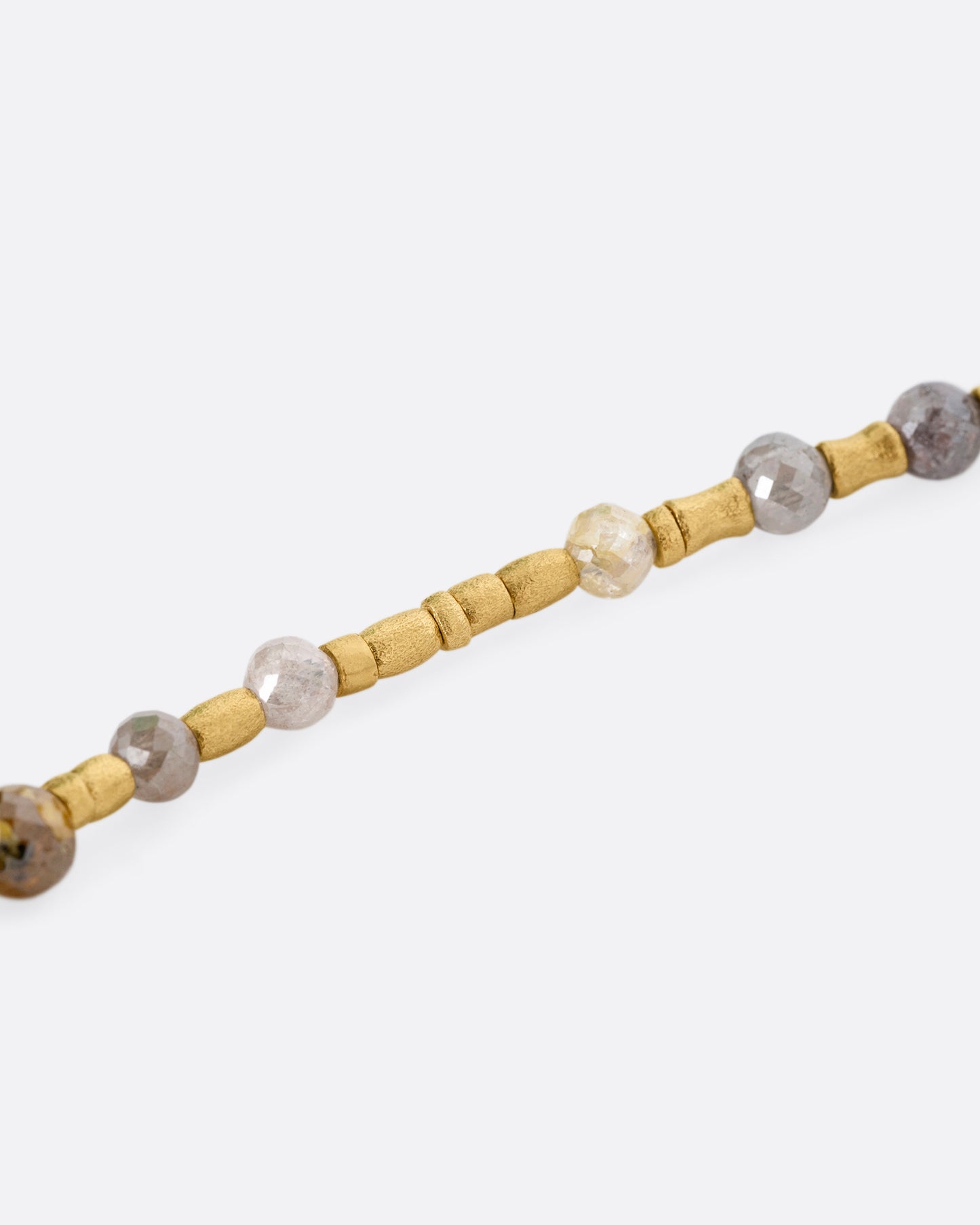 A close up of a multicolored diamond beaded necklace with a yellow gold charm holder.