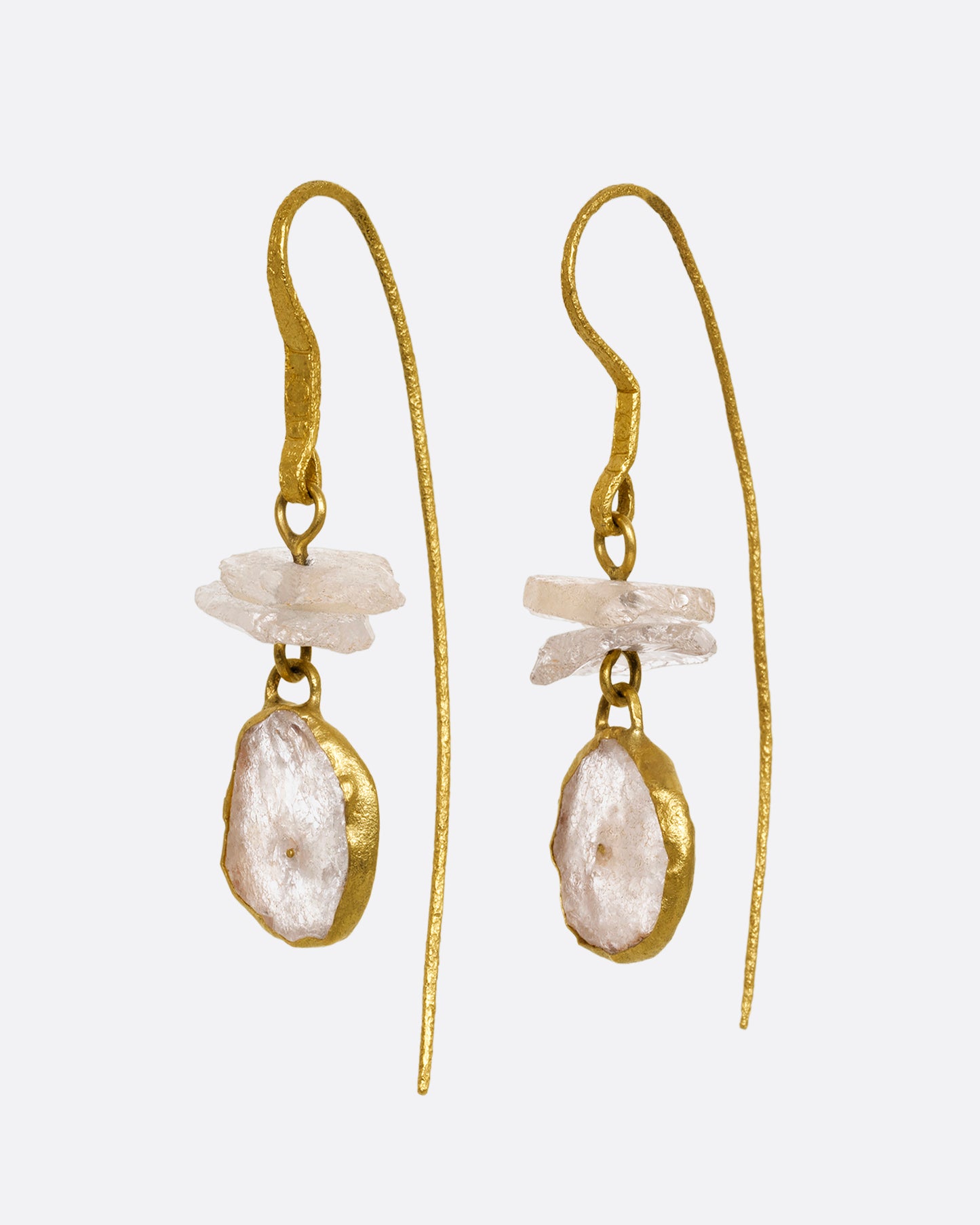 A pair of earrings with white quartz stacks, yellow gold ear hooks, and two front- facing gold wrapped quartz slices. Shown from the side.