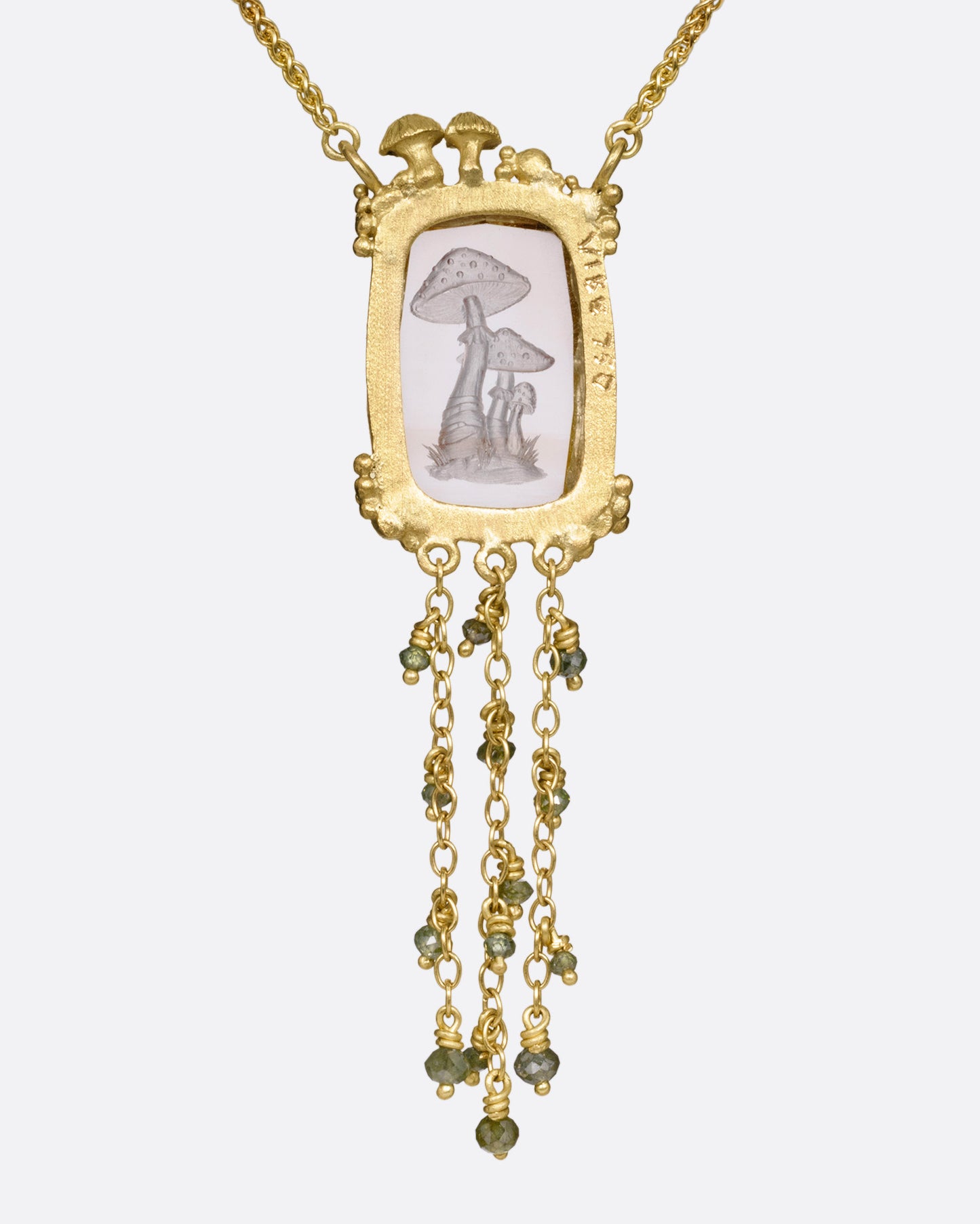 A yellow gold pendant necklace with a hand carved cluster of mushrooms in a light pink topaz with gold mushrooms and a diamond at the top edge. Three gold chains with green diamond beads hand from its base. Shown from the back.