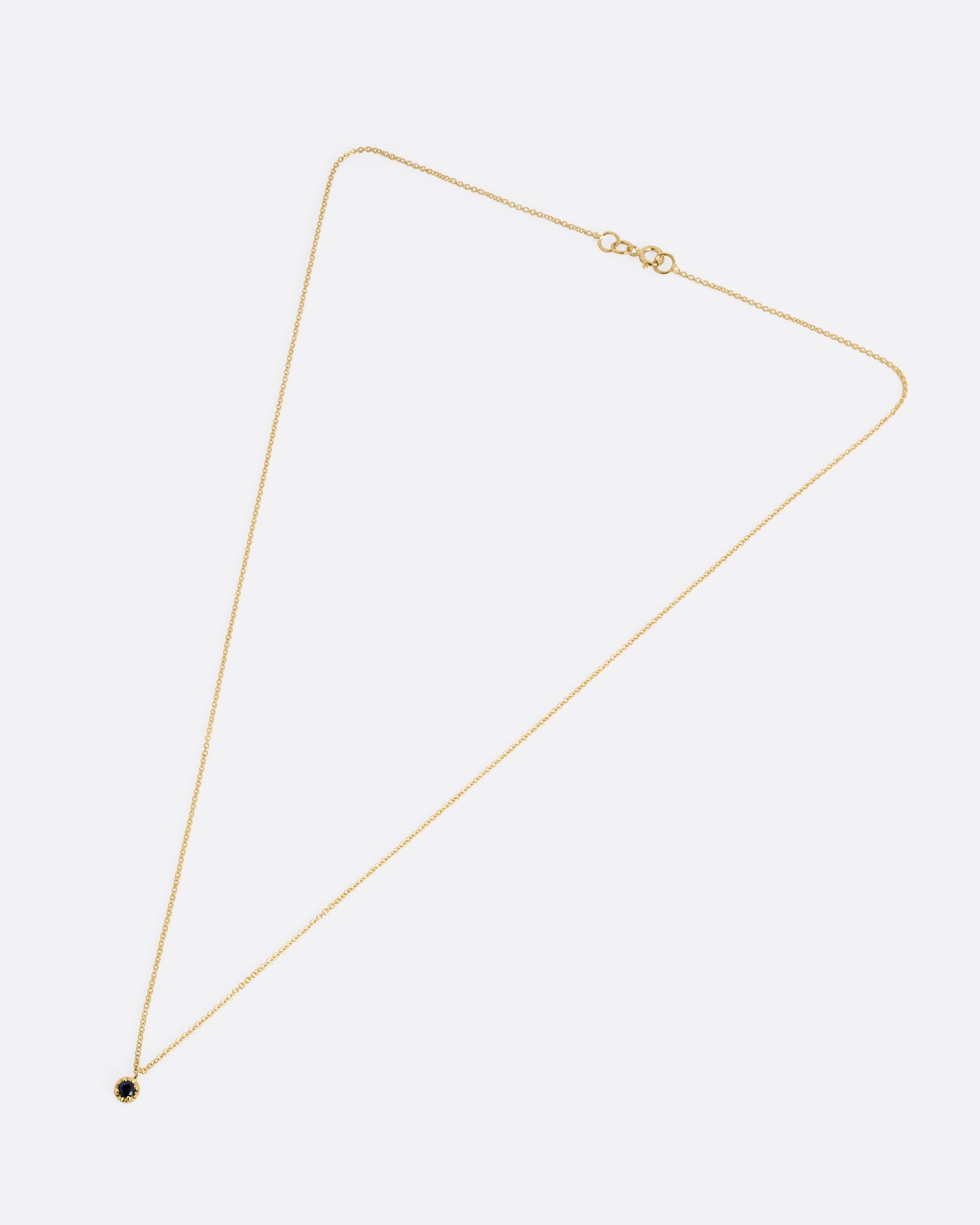 A yellow gold cable chain necklace with a prong set sapphire, shown from the front.