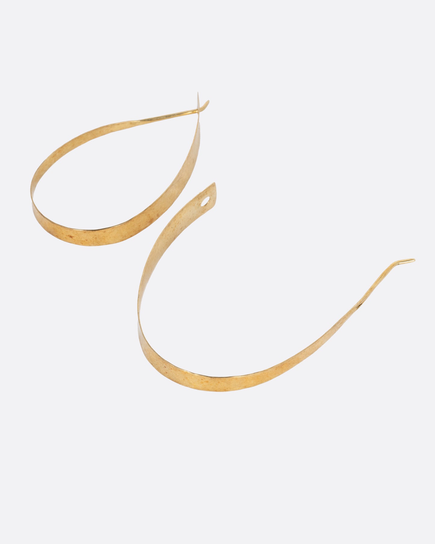 A pair of yellow gold loop earrings with a tapered silhouette and minimalist closure, shown lying flat with one earring open.