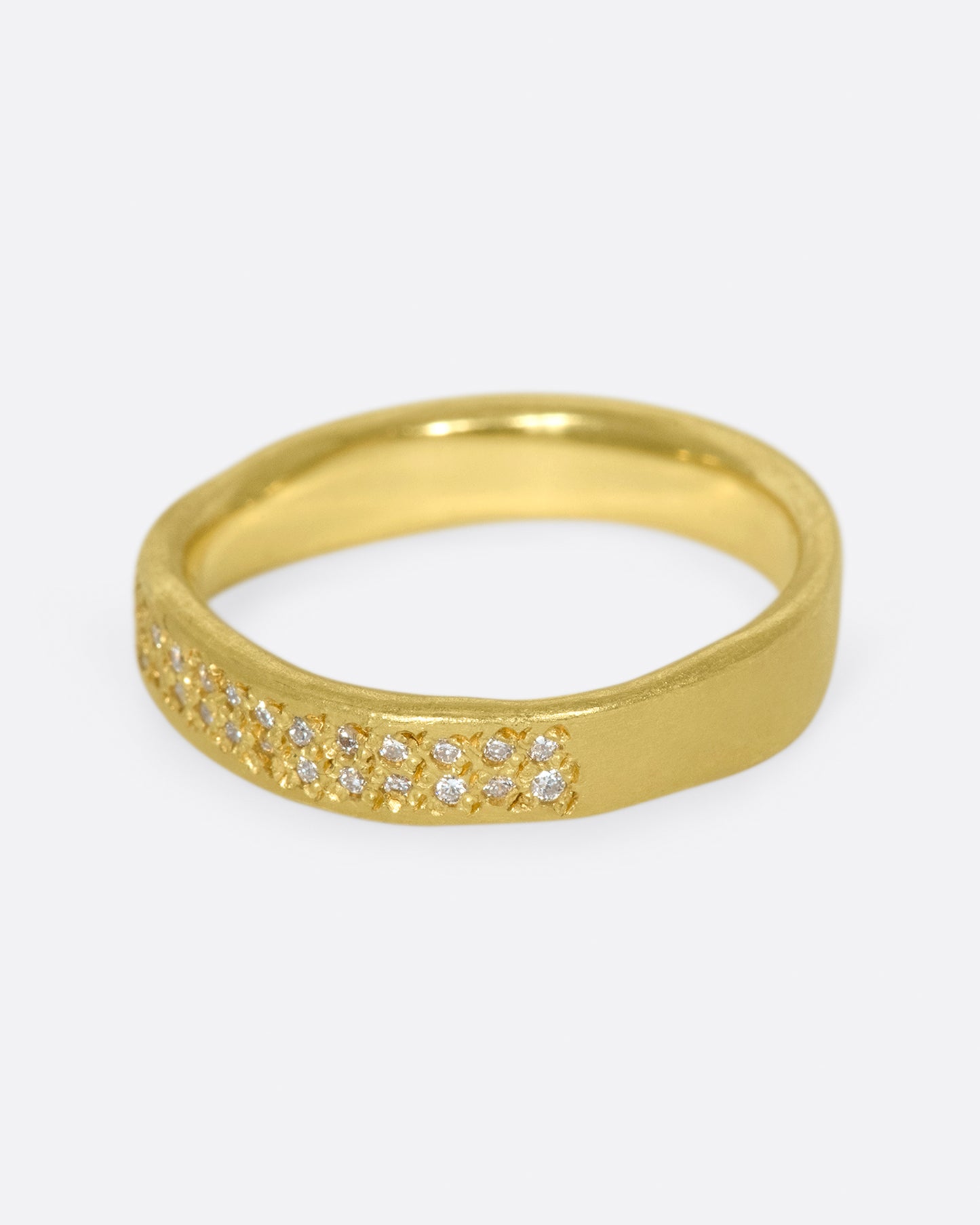 A hand-formed, brushed gold band with two rows of diamonds along half of it. Shown from the side.