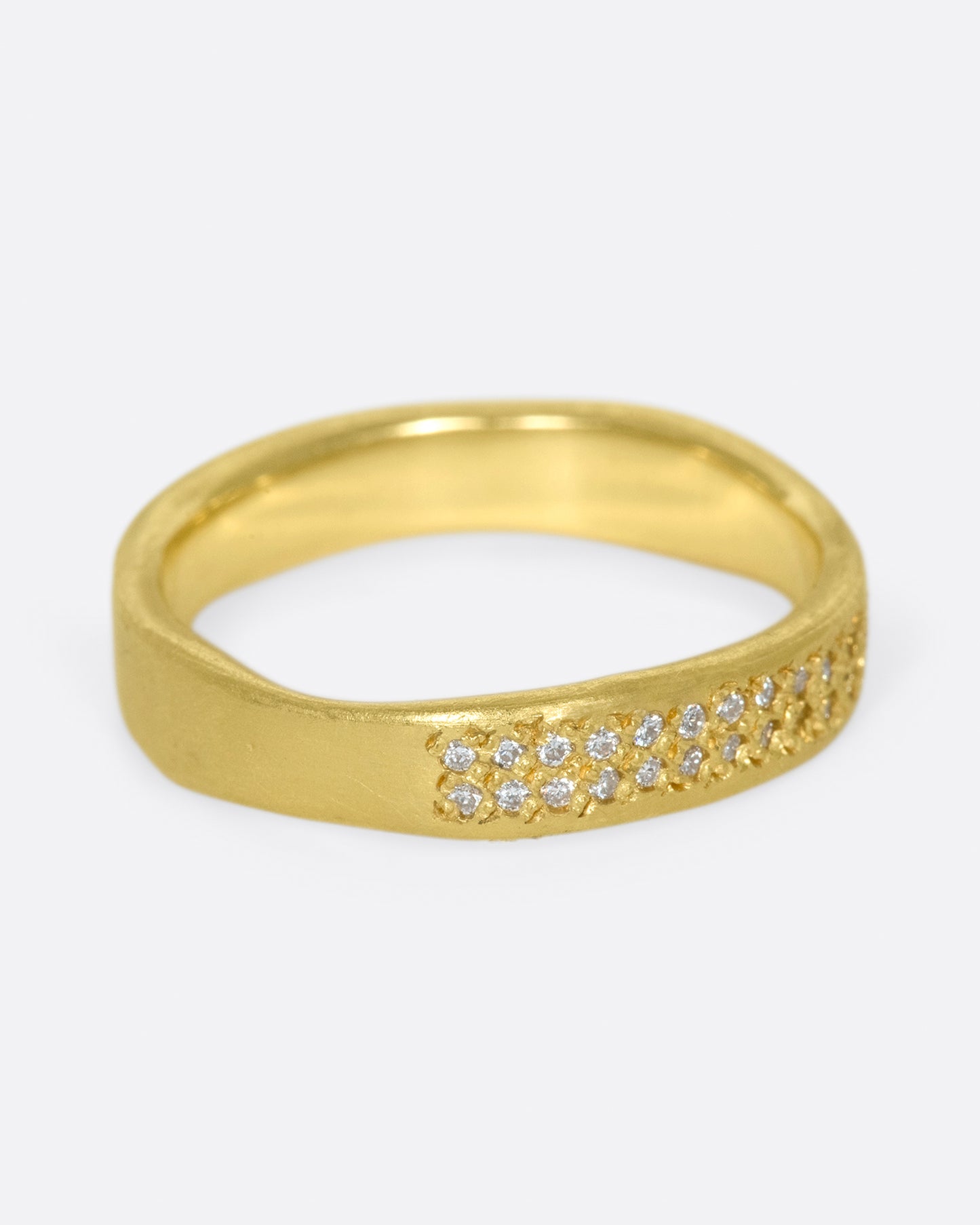 A hand-formed, brushed gold band with two rows of diamonds along half of it. Shown from the side.