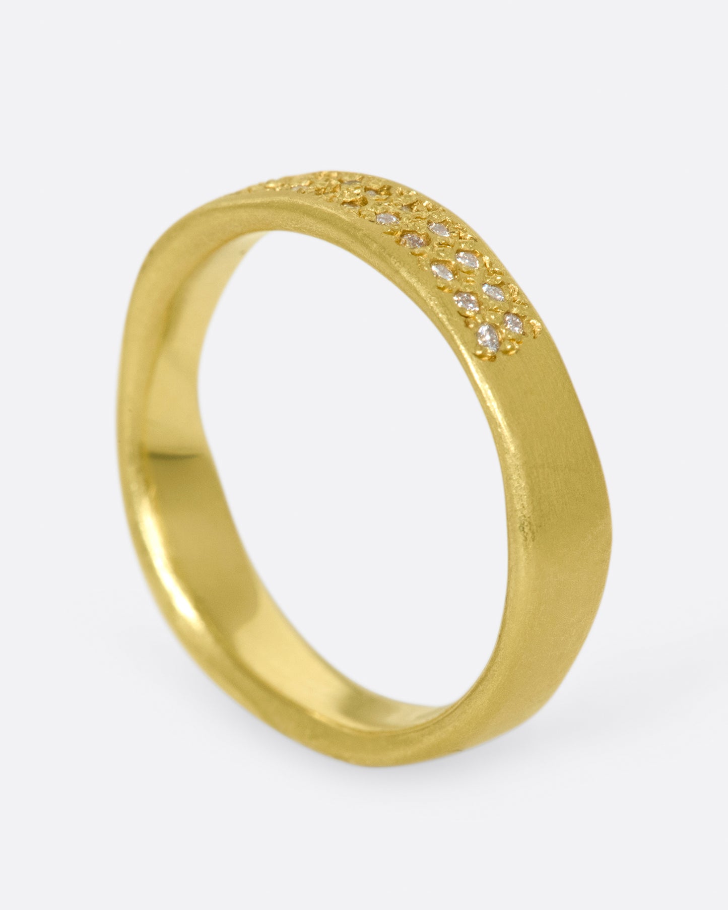 A hand-formed, brushed gold band with two rows of diamonds along half of it. Shown standing from the side.