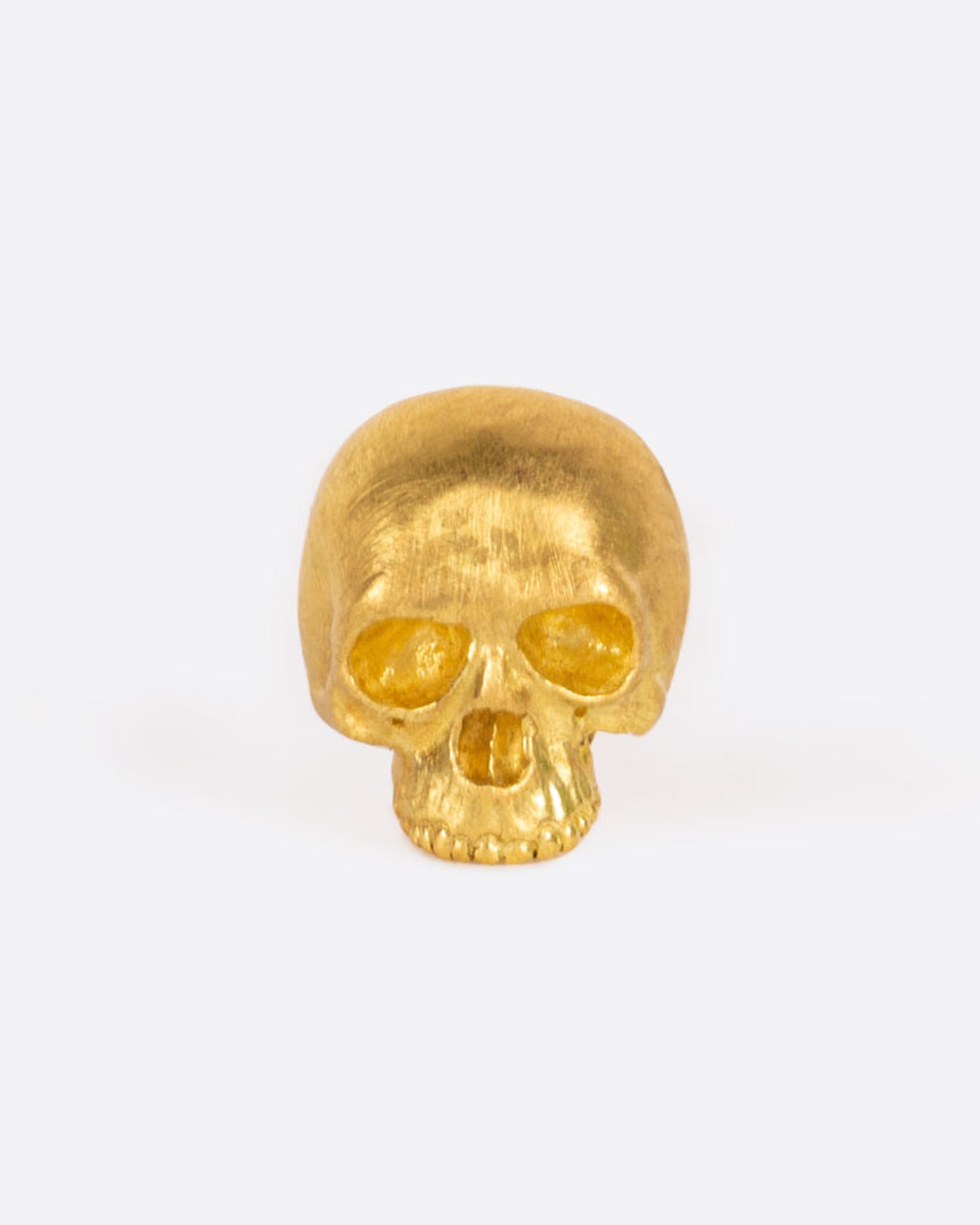 A solid yellow gold skull stud earring. Shown from the front.