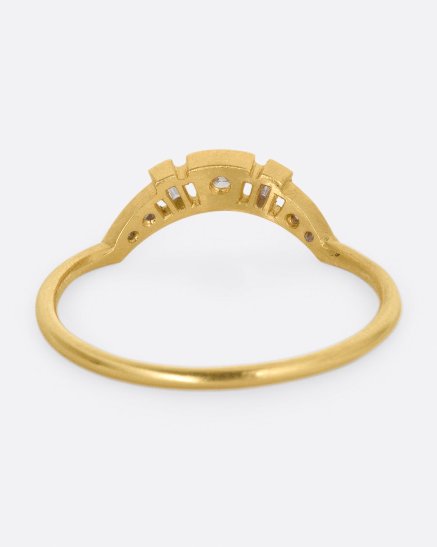 A yellow gold ring with a curved face that makes it good for stacking, dotted with round and baguette diamonds, and milgrain details - shown from the back.