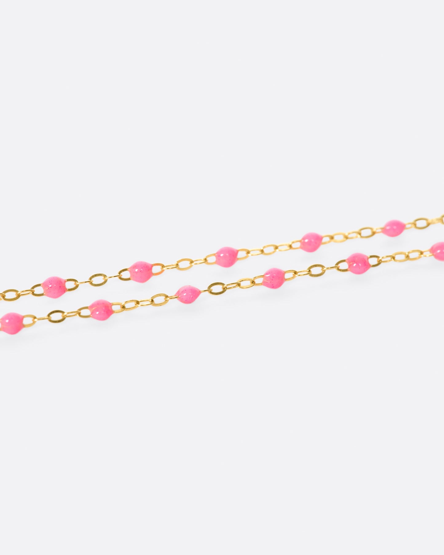 A close up view of a yellow gold cable chain necklace with pink resin droplets. Shown from the side.