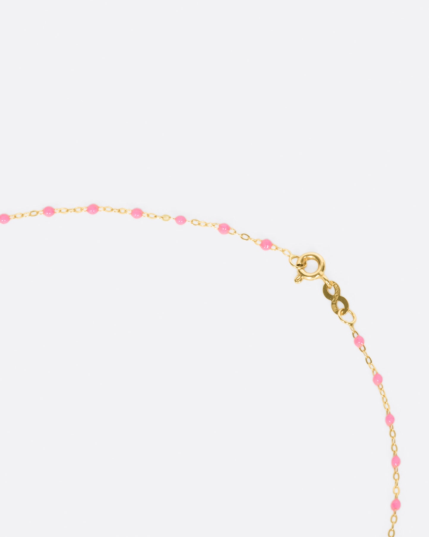 A close up view of a yellow gold cable chain necklace with pink resin droplets and its clasp. Shown from the side.