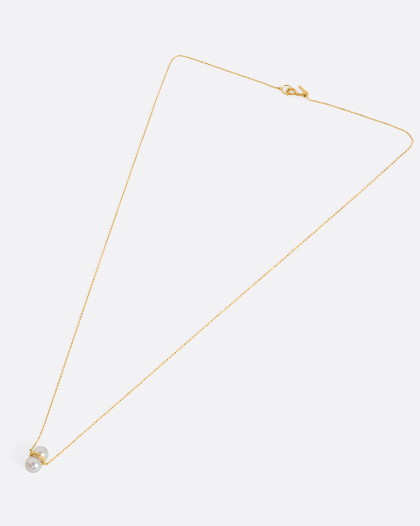 Two large pearls are paired vertically with a gold setting, and attached to a gold necklace. View from above, laying flat.