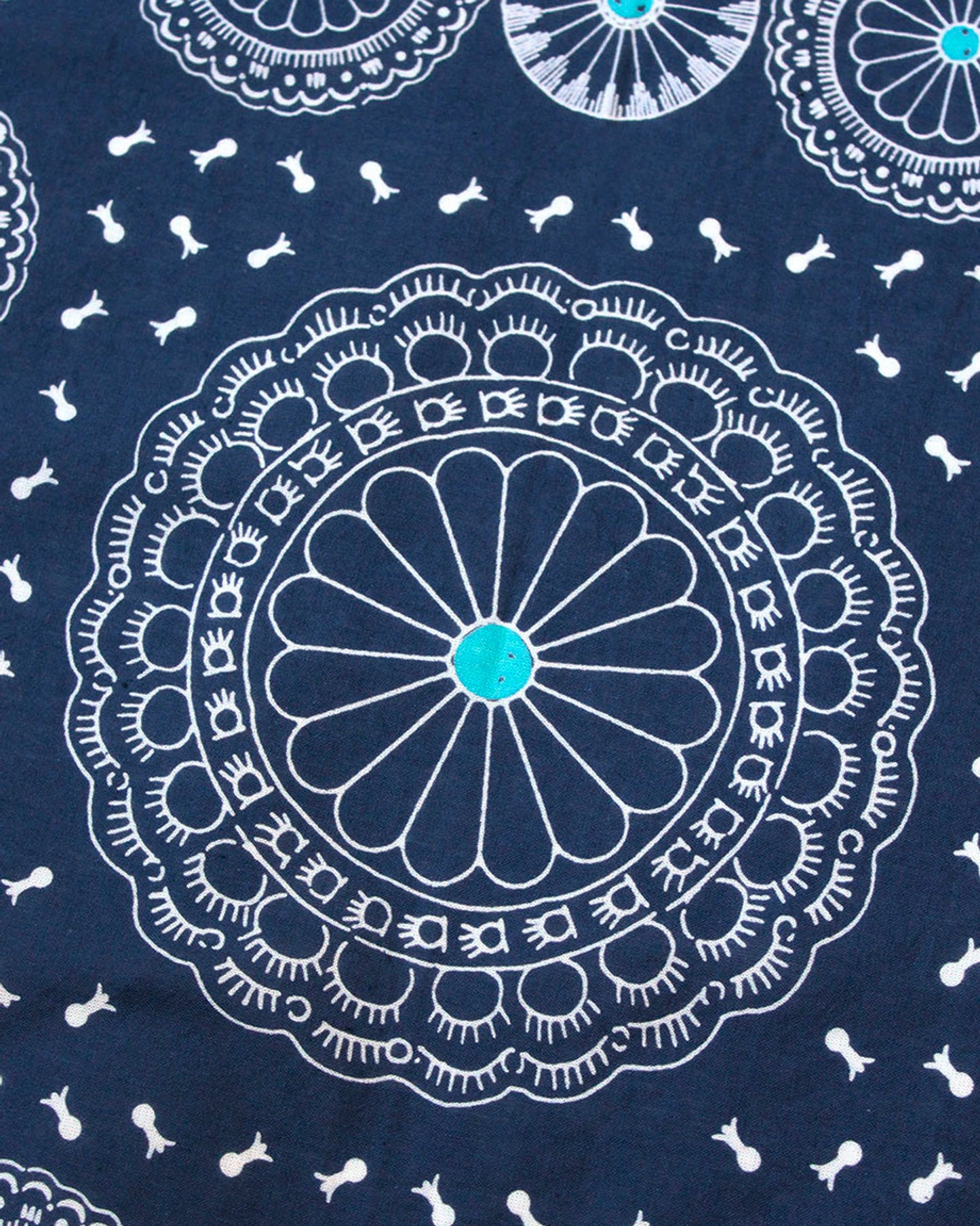 A close up of a navy selvedge bandana with a pattern of turquoise- centered conchos.