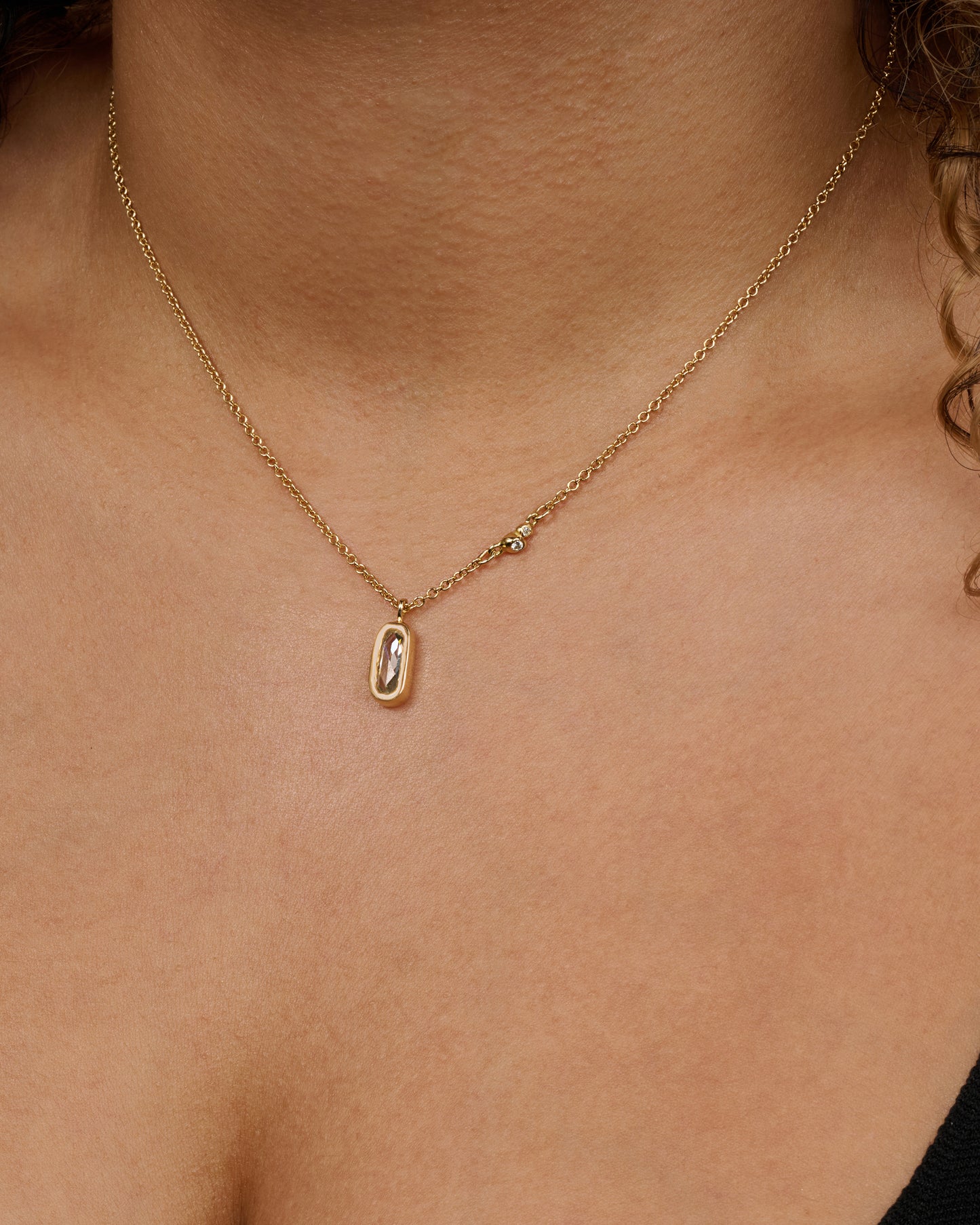 A yellow gold necklace with a rose cut solitaire diamond pendant and a cluster of diamonds on the chain. View of the necklace worn.