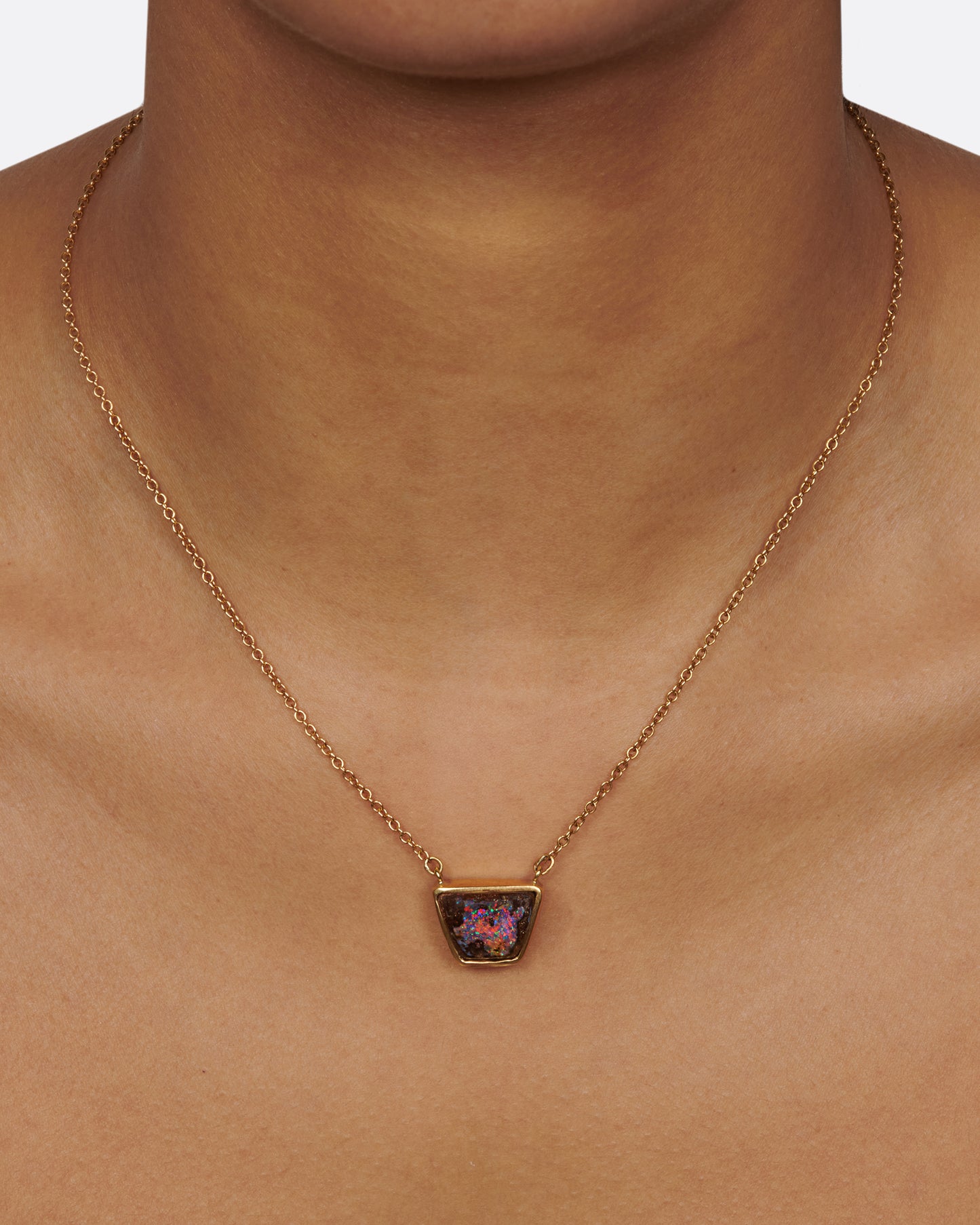 A yellow gold cable chain necklace with a trapezoidal opal set in a bezel. Shown from the front on a person.