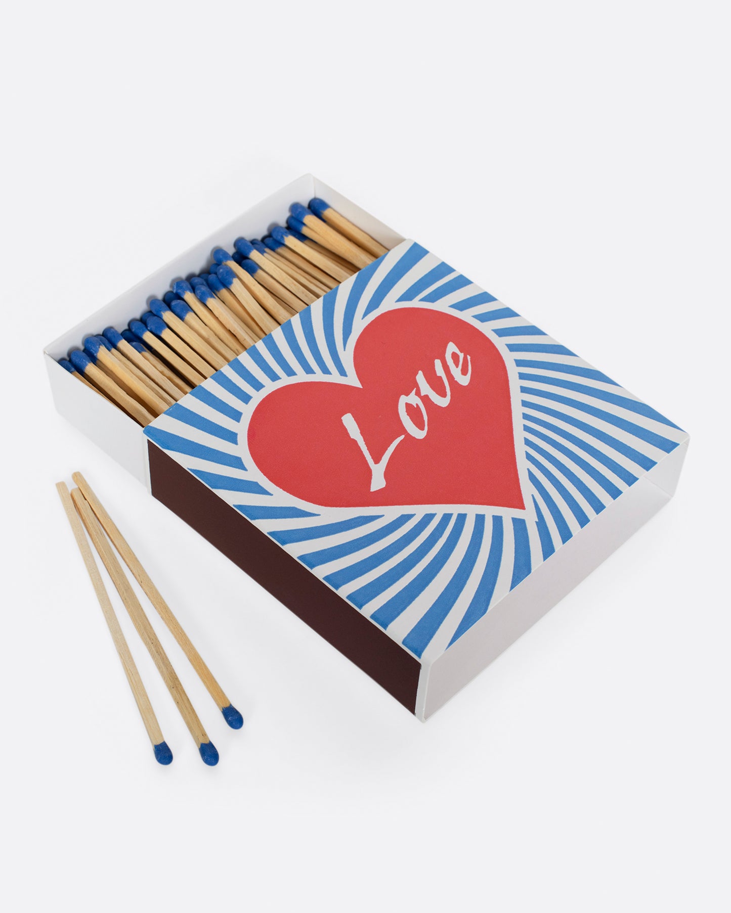 An open matchbox with blue tipped wooden matches. The cover has a red heart with 'Love' at the center, surrounded by blue and white swirls. Shown at an angle from the top with three matches at its side.