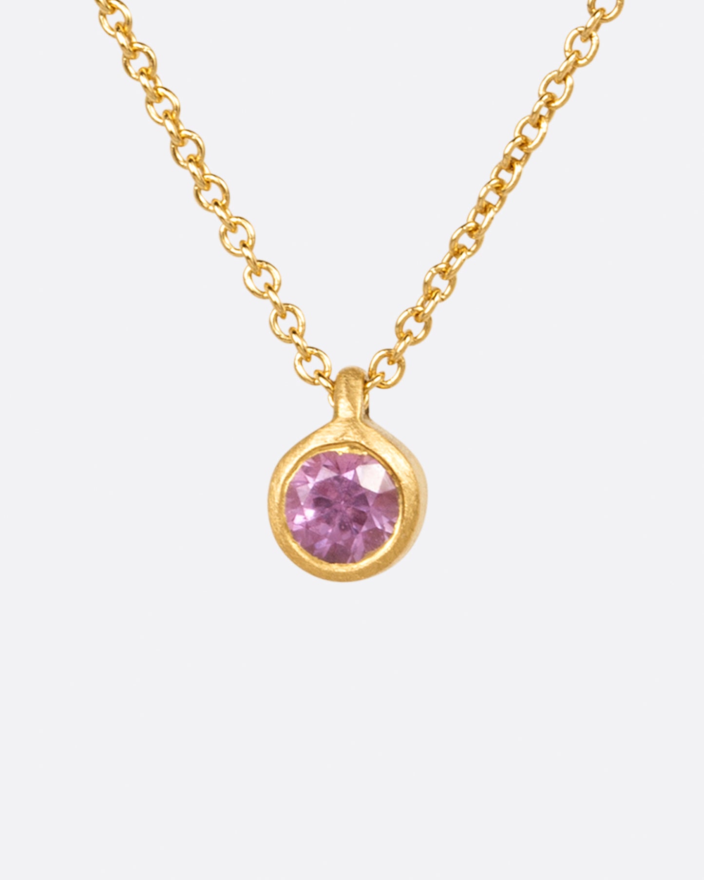A rosy pink sapphire pendant set in a matte yellow gold bezel