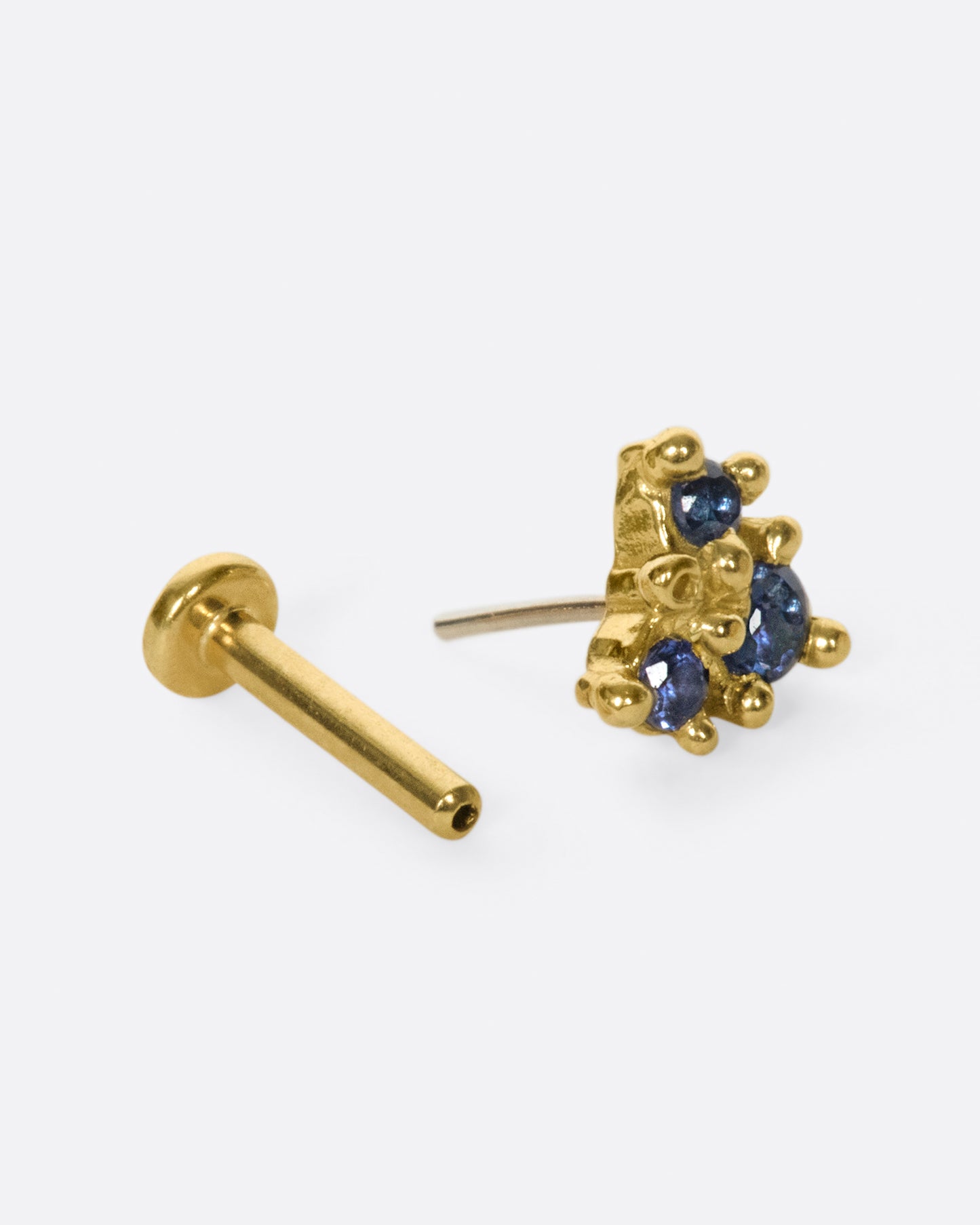 An arrow-like shape with three blue sapphires set in hand formed prongs.