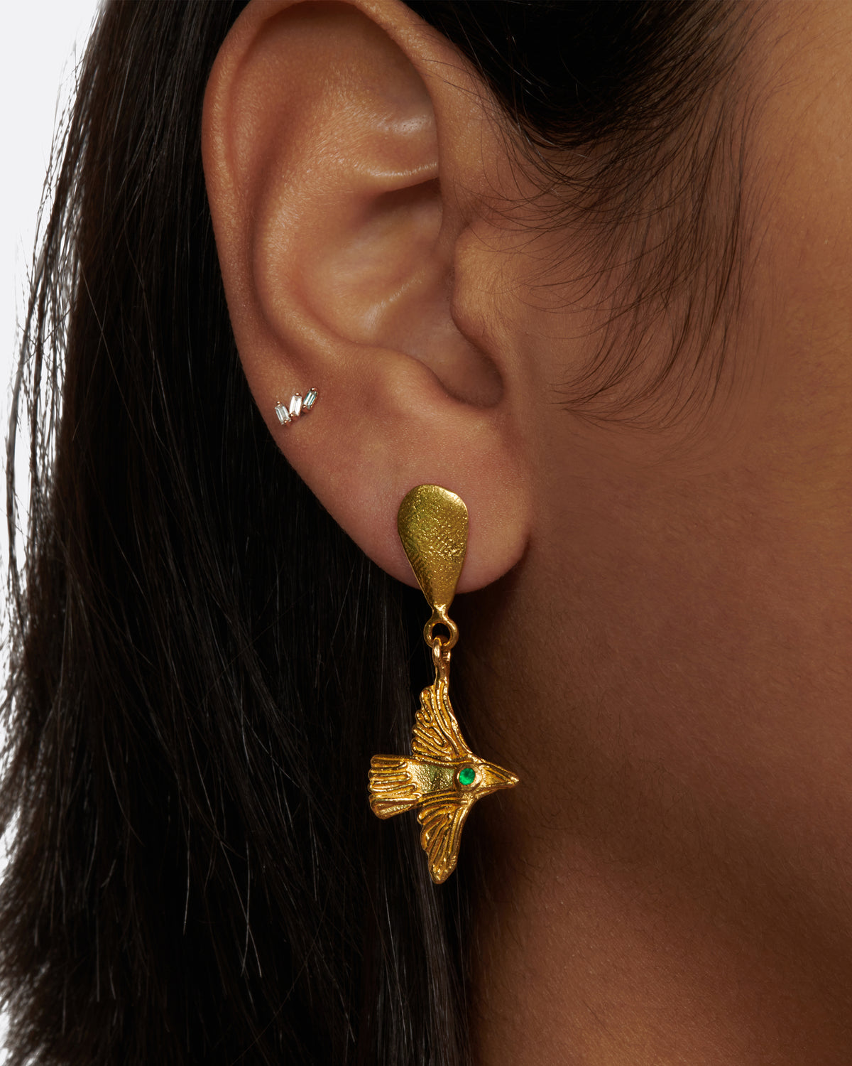 Yellow gold bird earrings with emerald eyes, a bird earring worn on an ear