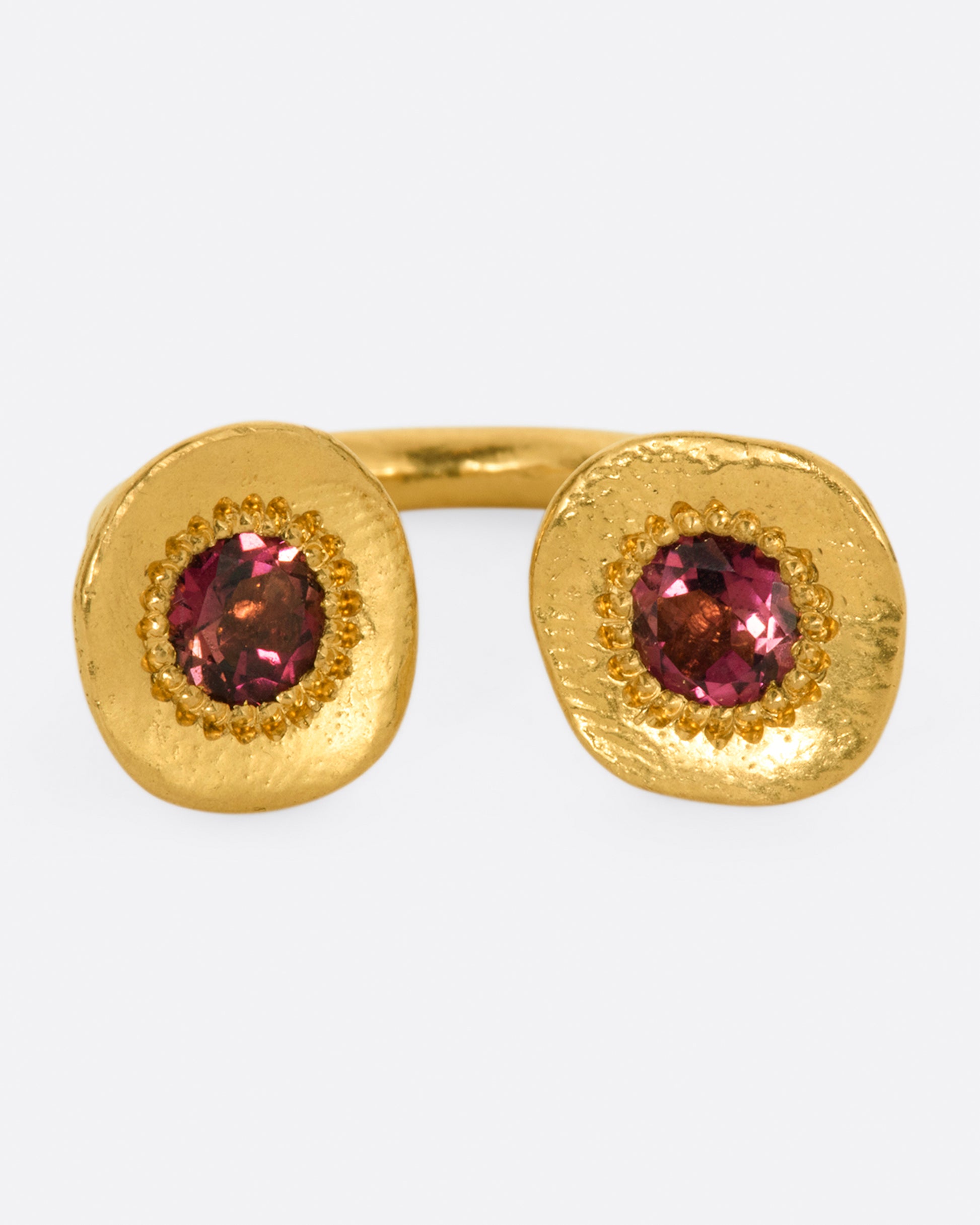 A high karat gold open ring with a large organic shaped disc on each end with a rosey pink tourmaline at its center.
