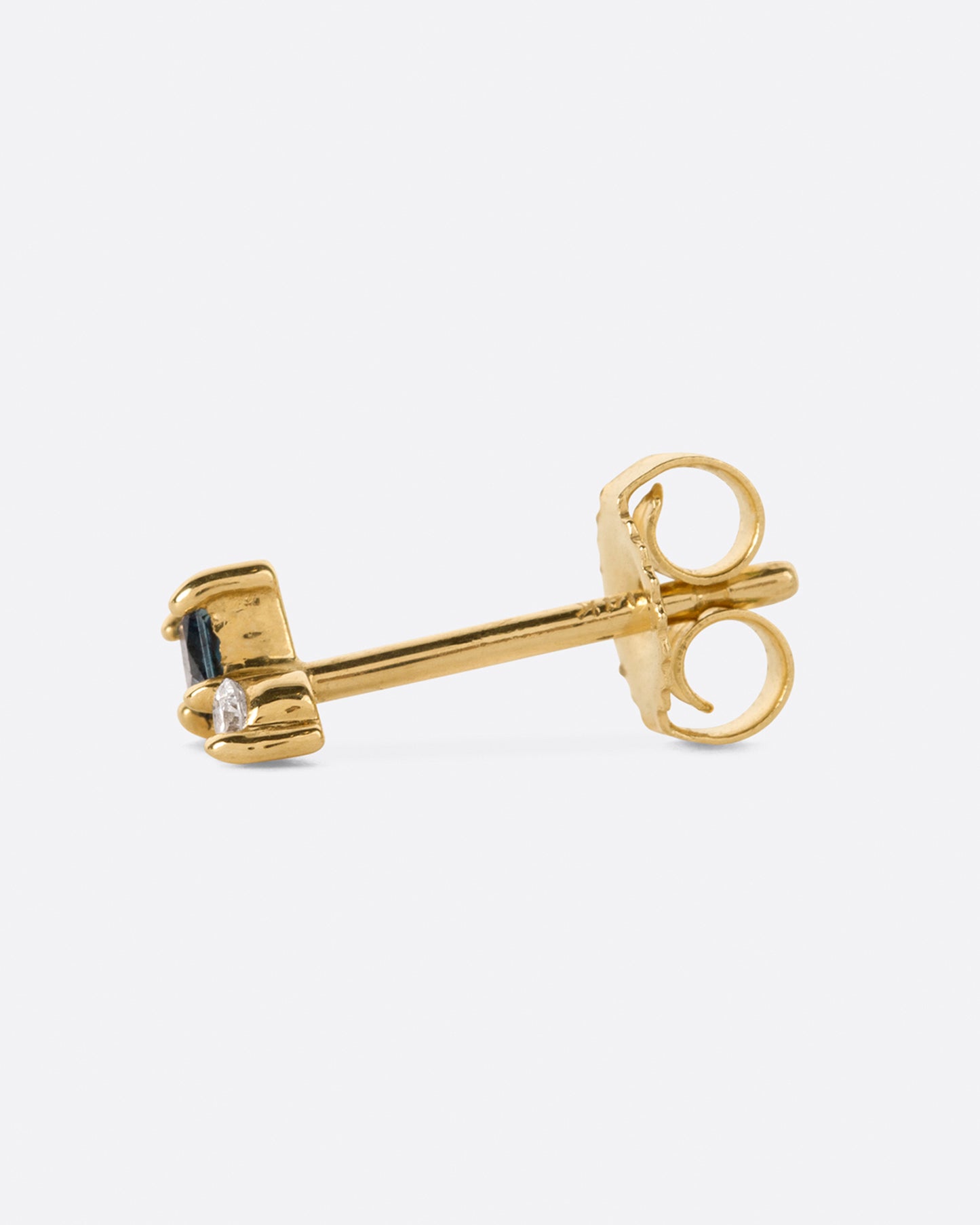 A yellow gold stud earring with a prong set round diamond sitting atop a princess cut teal blue sapphire. Shown on its side from the side.