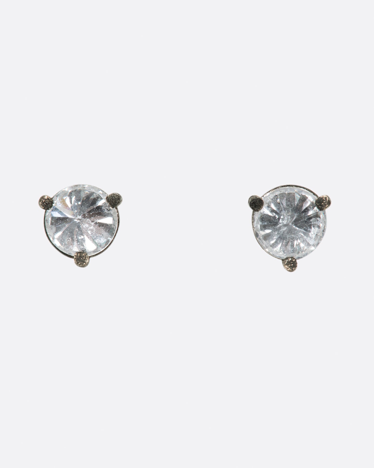 A pair of solitaire stud earrings with round inverted diamonds set in darkened white gold settings. Shown from the front.