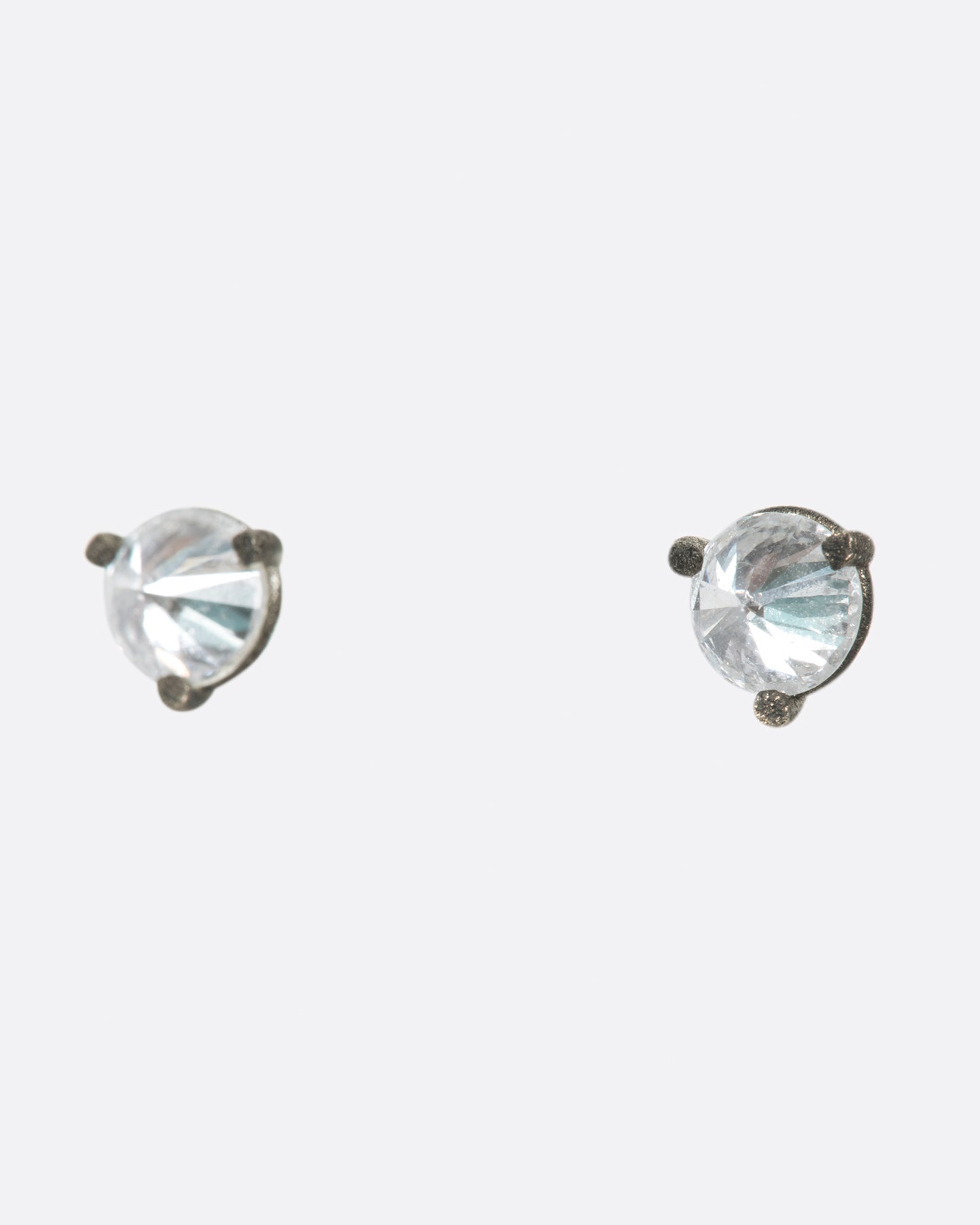 A pair of solitaire stud earrings with round inverted diamonds set in darkened white gold settings. Shown from the side.
