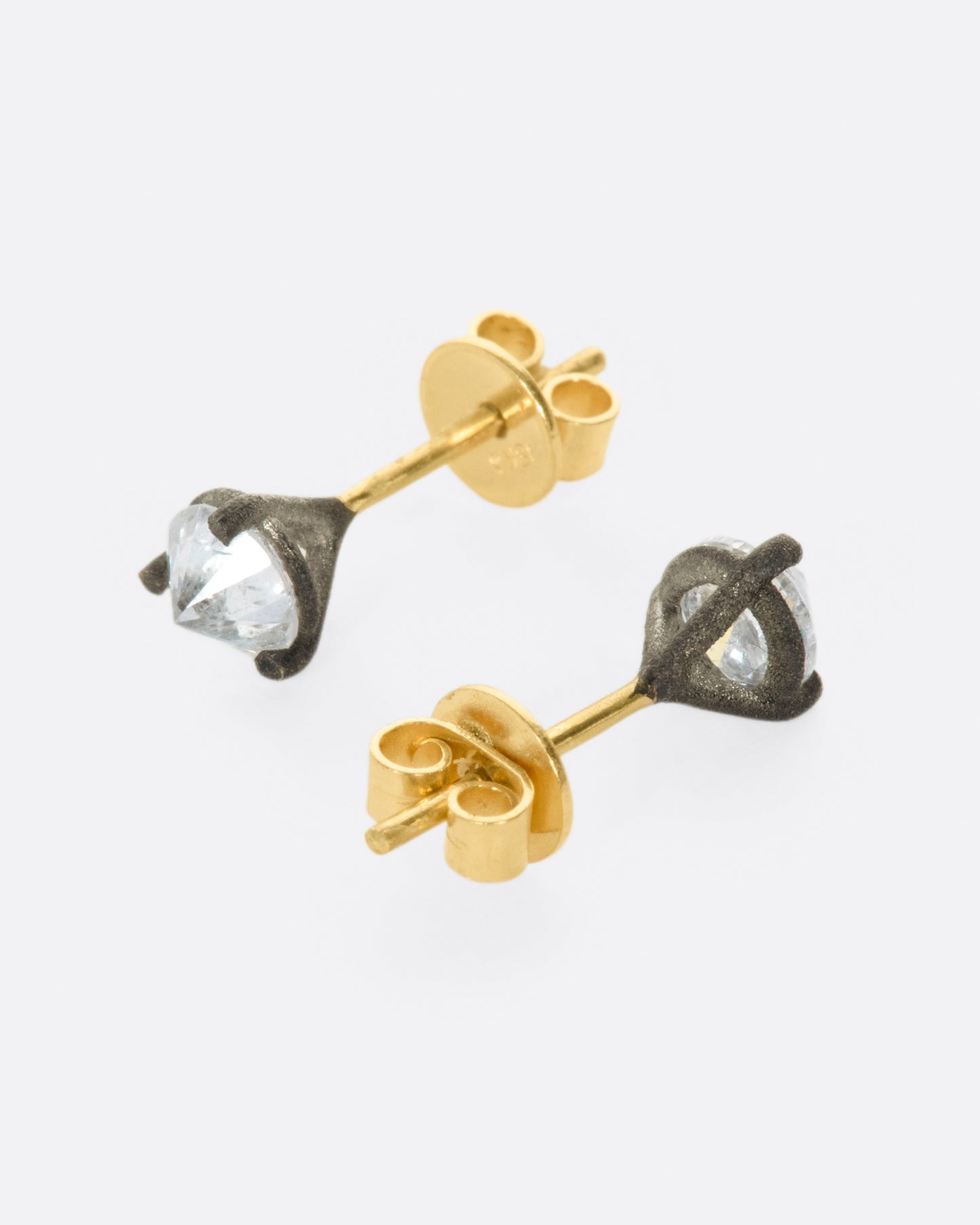 A pair of solitaire stud earrings with round inverted diamonds set in darkened white gold settings. One earring is shown from the side lying flat facing front, the other is shown facing back.