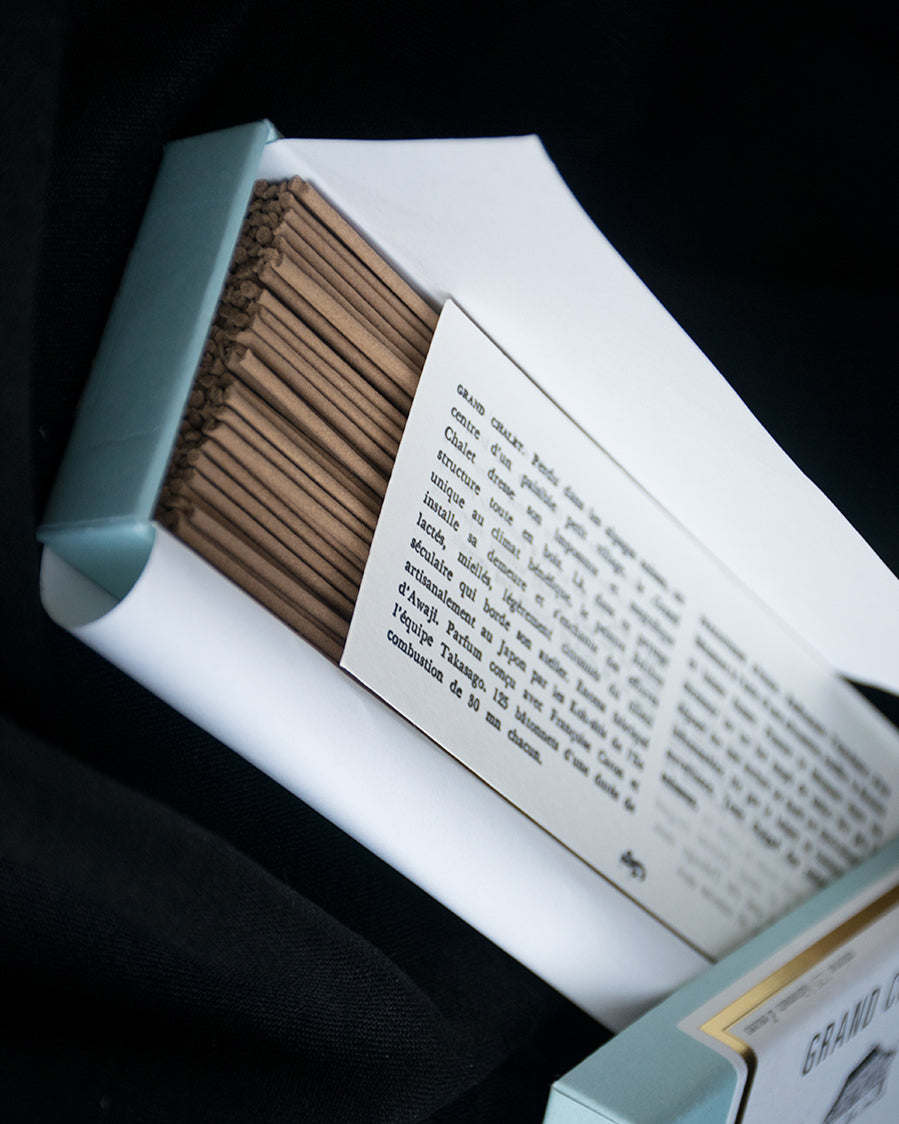 An open box of incense, revealing incense sticks and the included literature as well as the turquoise, white, and metallic gold packaging. Shown diagonally from the top.