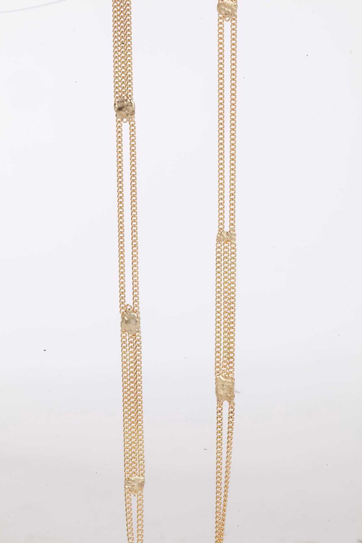 A long yellow gold multi chain necklace with alternating pattern of squares finished with gold solder. Shown close up from the front.