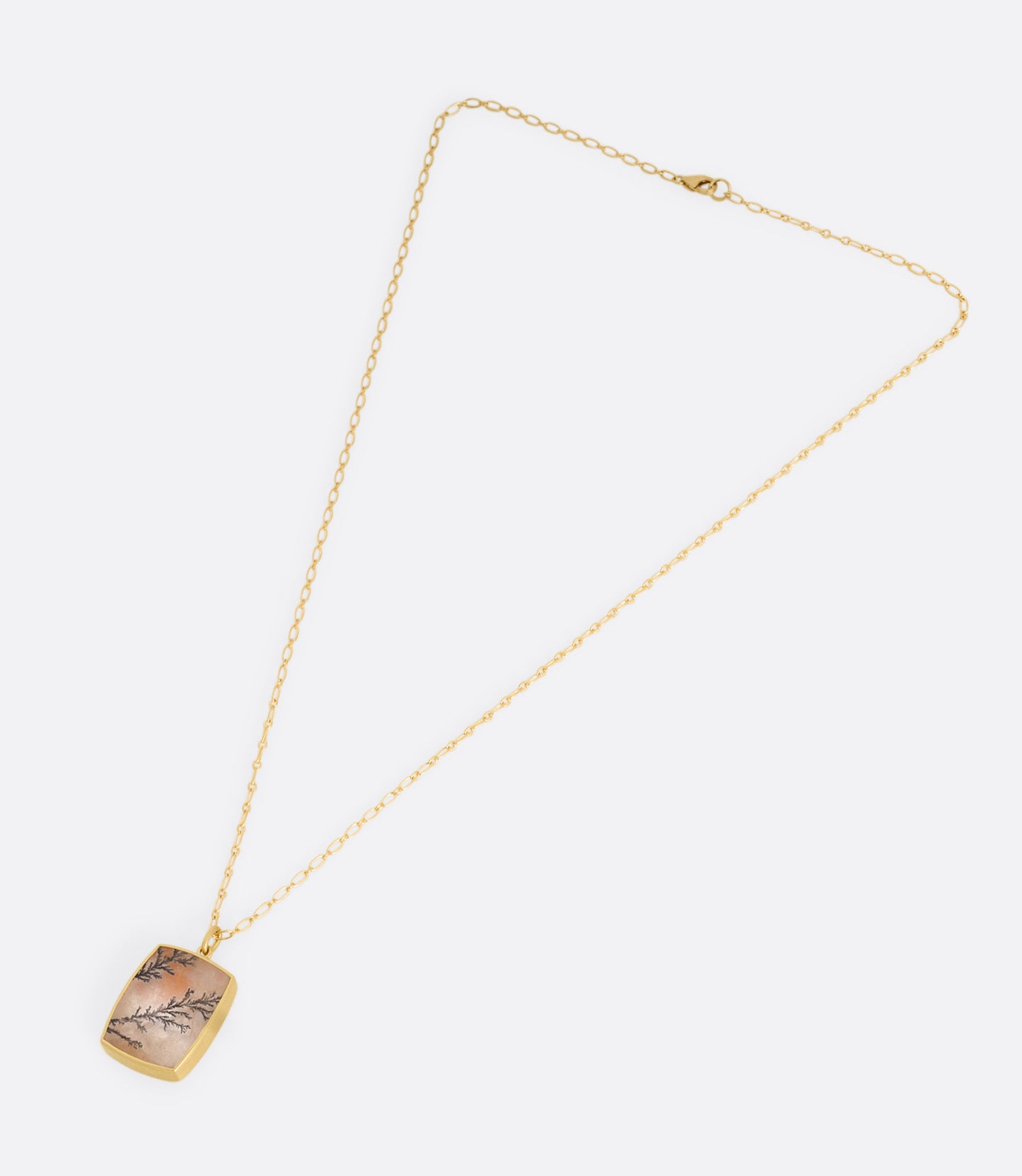 A yellow gold dendritic quartz pendant hanging from an alternating oval chain. Shown laying flat.