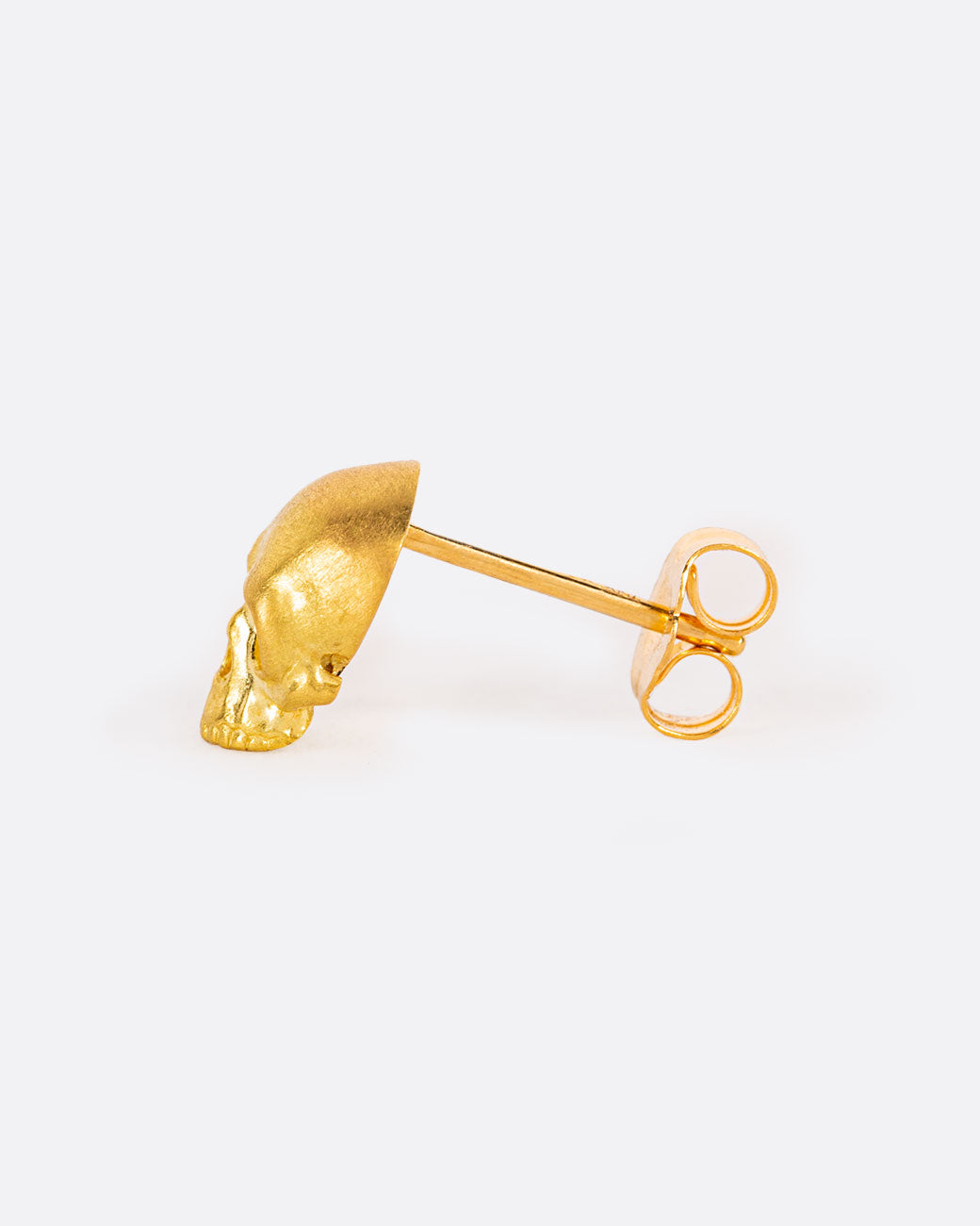 A solid yellow gold skull stud earring. Shown from the side.