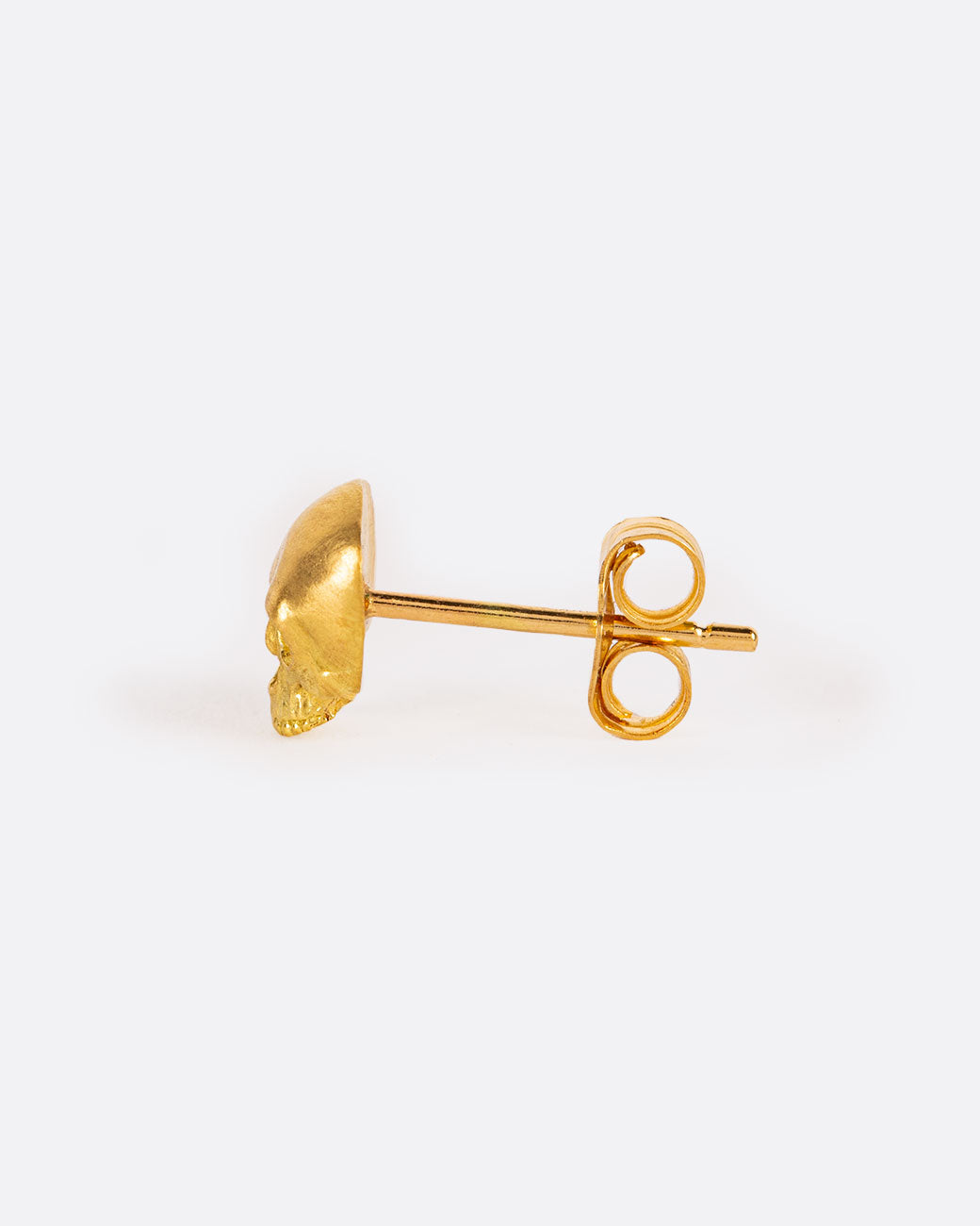 A solid yellow gold skull stud earring. Shown from the side.