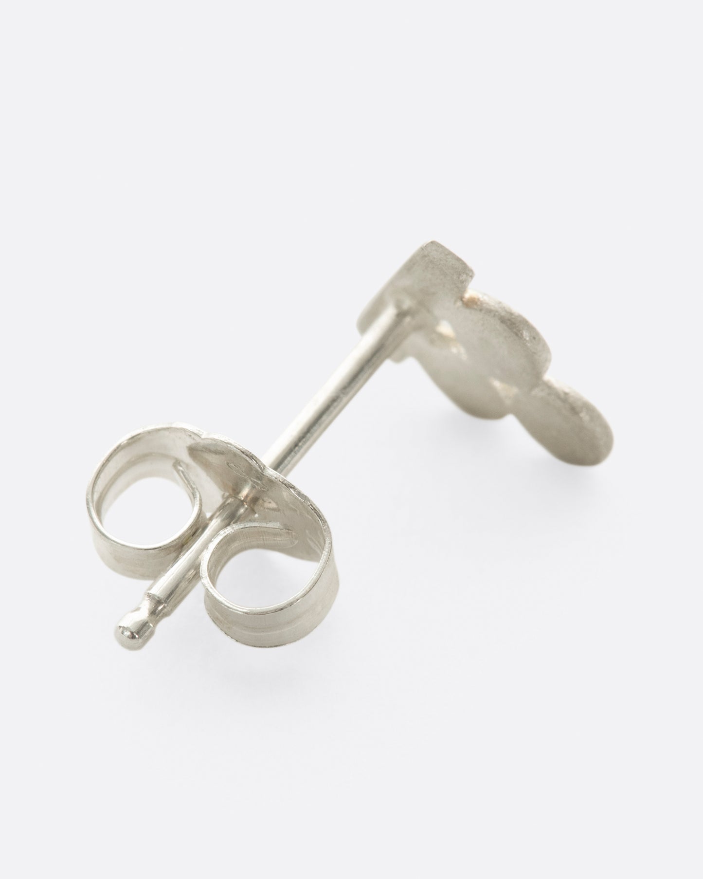 A silver stud earring with three matte circles sitting on a bar. Shown lying flat from the back.