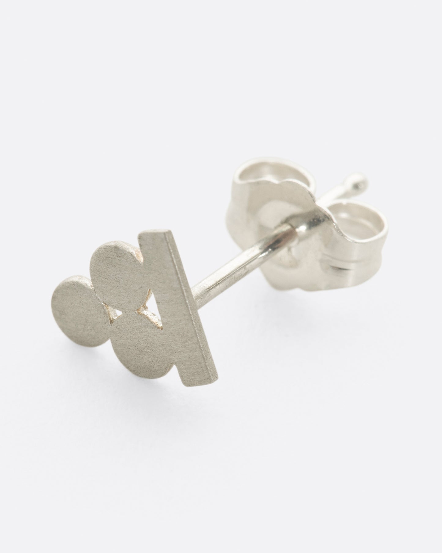 A silver stud earring with three matte circles sitting on a bar. Shown lying flat from the side.