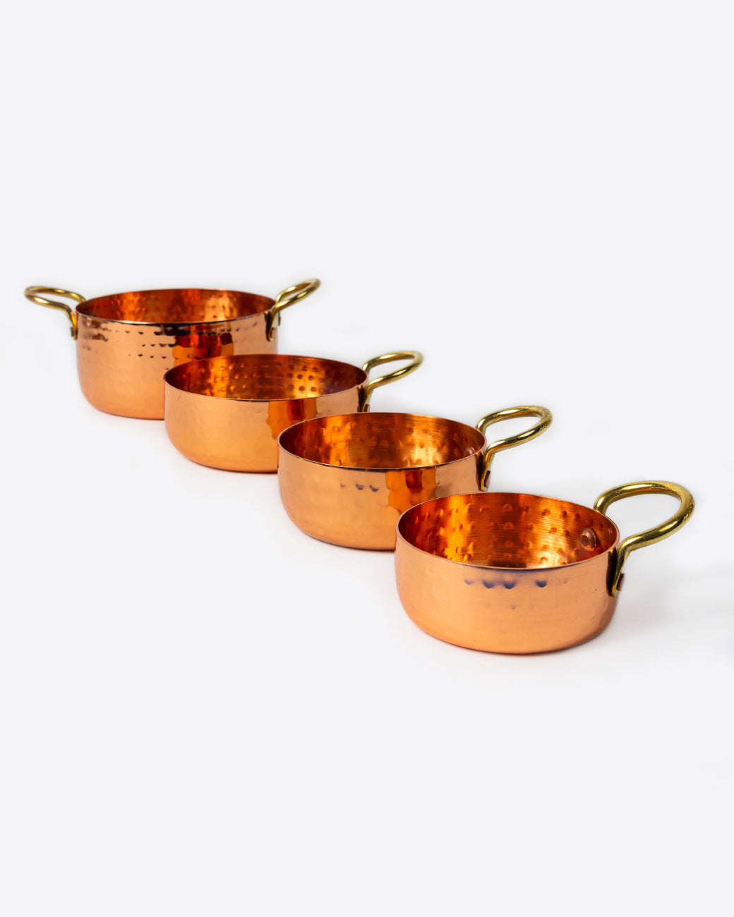 A set of four hammered copper measuring cups sitting next to one each other. Shown from the front at an angle.