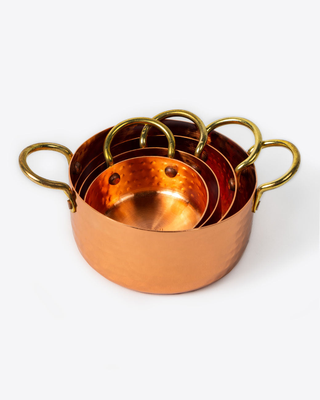 A set of four hammered copper measuring cups, stacked together. Shown from the front.