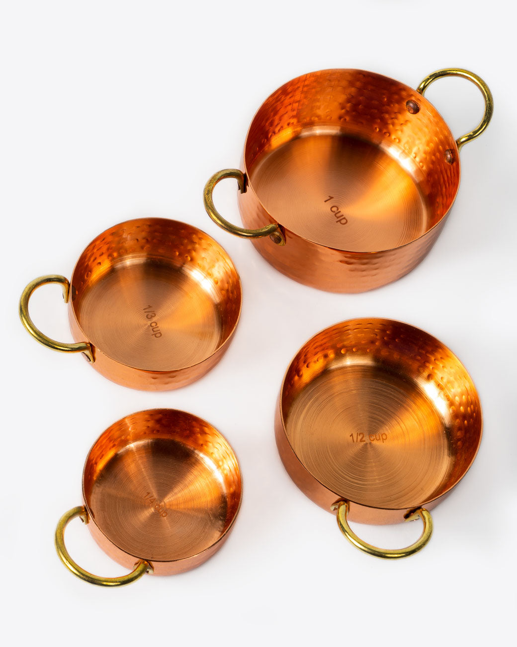 A set of four hammered copper measuring cups, shown from above.