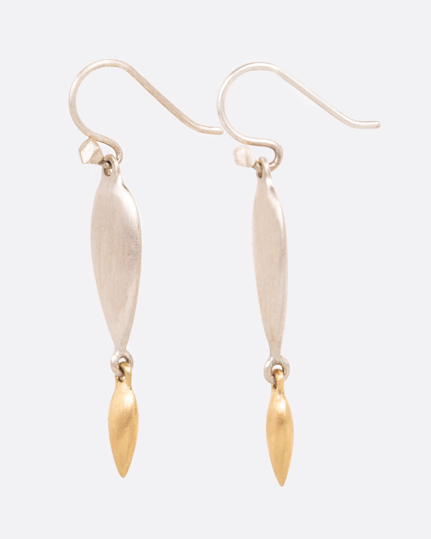 A pair of sterling silver teardrop earrings with yellow gold teardrop dangles at the bottom. Shown from the side.