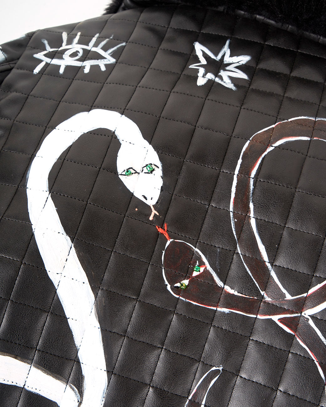 A close up of a hand painted black and white checked jacket with a faux fur collar and two snakes on the back. Shown from the back.