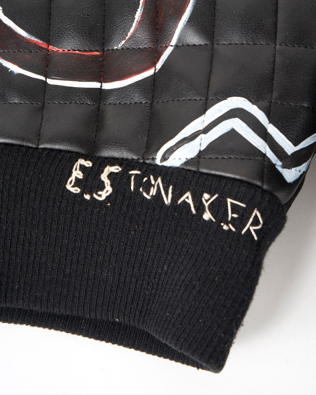 A close up of the artist's signature on a hand painted black and white jacket two snakes on the back. Shown from the back.