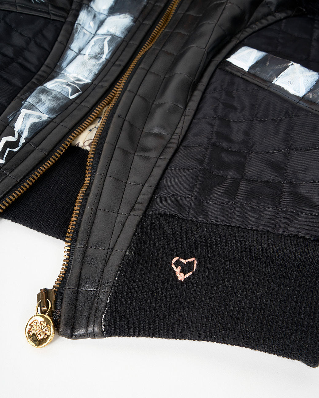 A close up of a hand painted black and white checked jacket with a faux fur collar and zip front. Shown from the front.