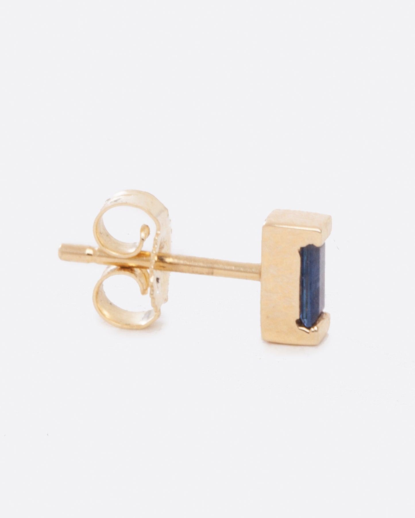 A small yellow gold single earring with a blue sapphire baguette. Shown from the side with the butterfly backing visible.