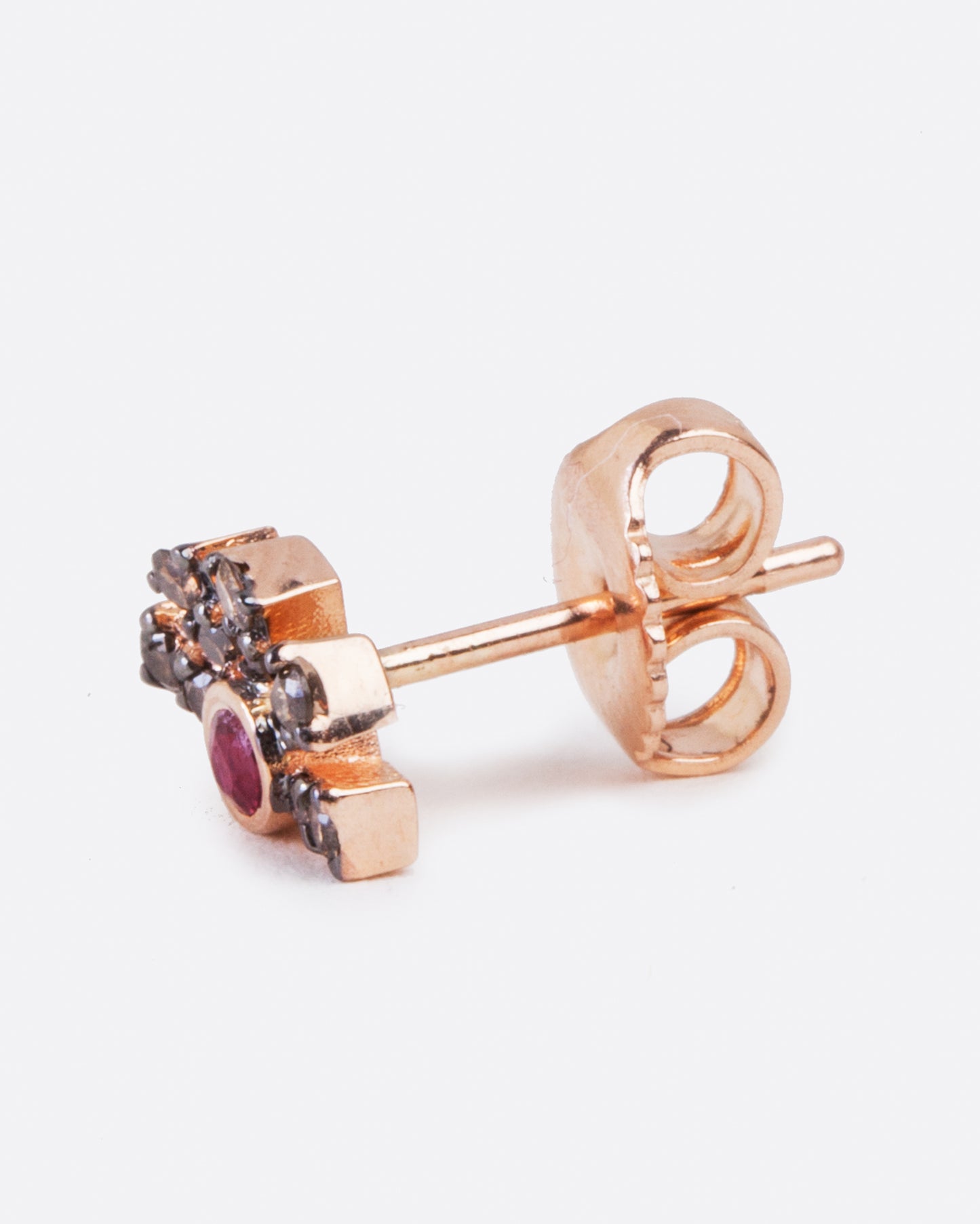 A single rose gold earring with a ruby in the middle and five black diamond pave bars extending from the ruby. Shown from the side with a butterfly backing on post.