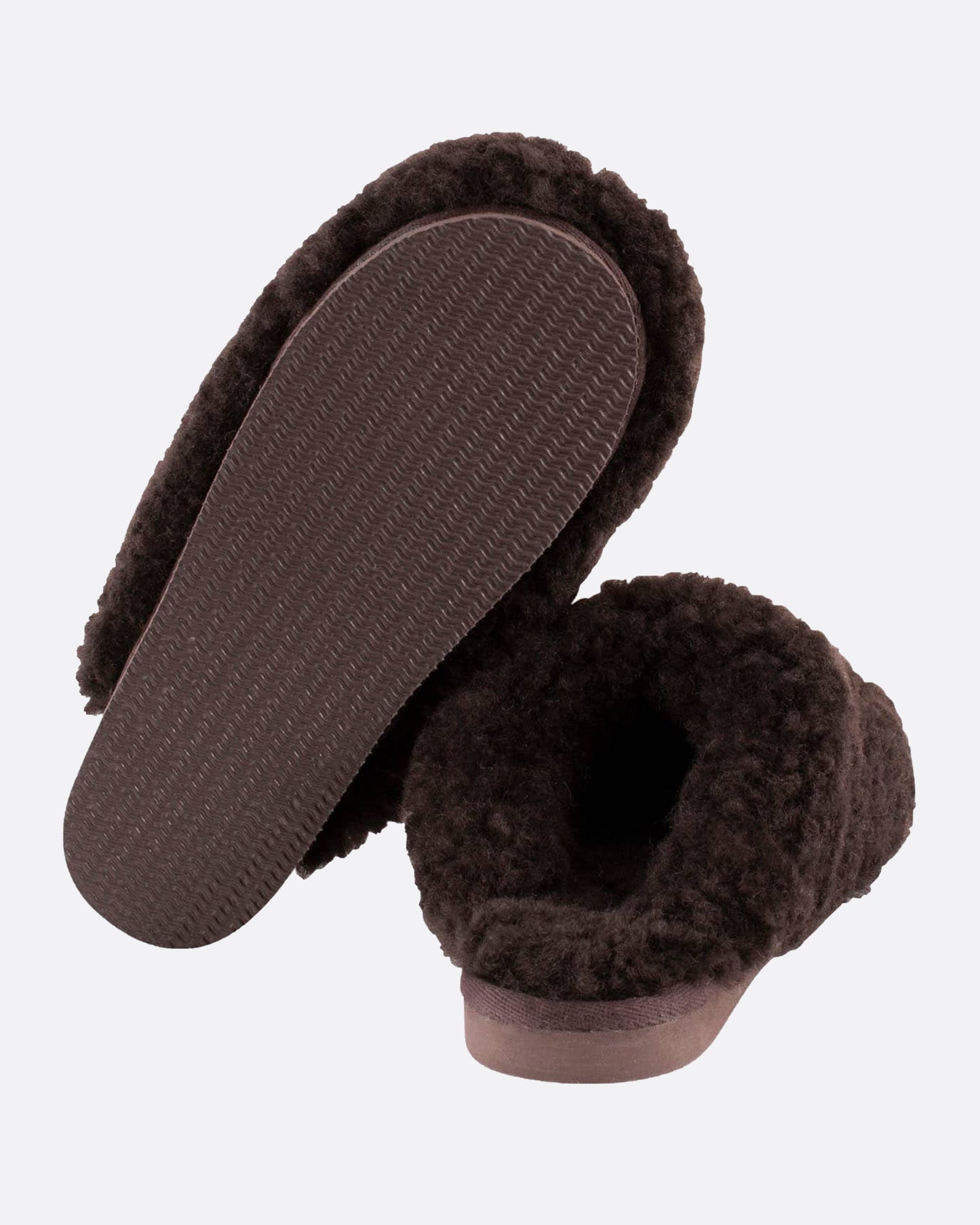 A pair of dark brown sheepskin slippers, shown from the back. One slipper is standing up so you can see the bottom.
