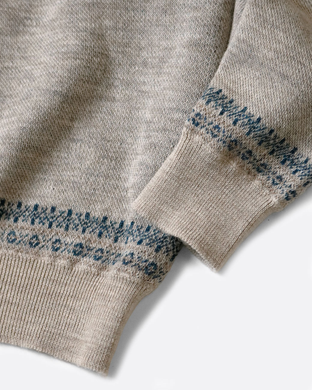 A close up of the cuff and bottom hem of a gray and navy crew neck sweater. Shown lying flat from the front.